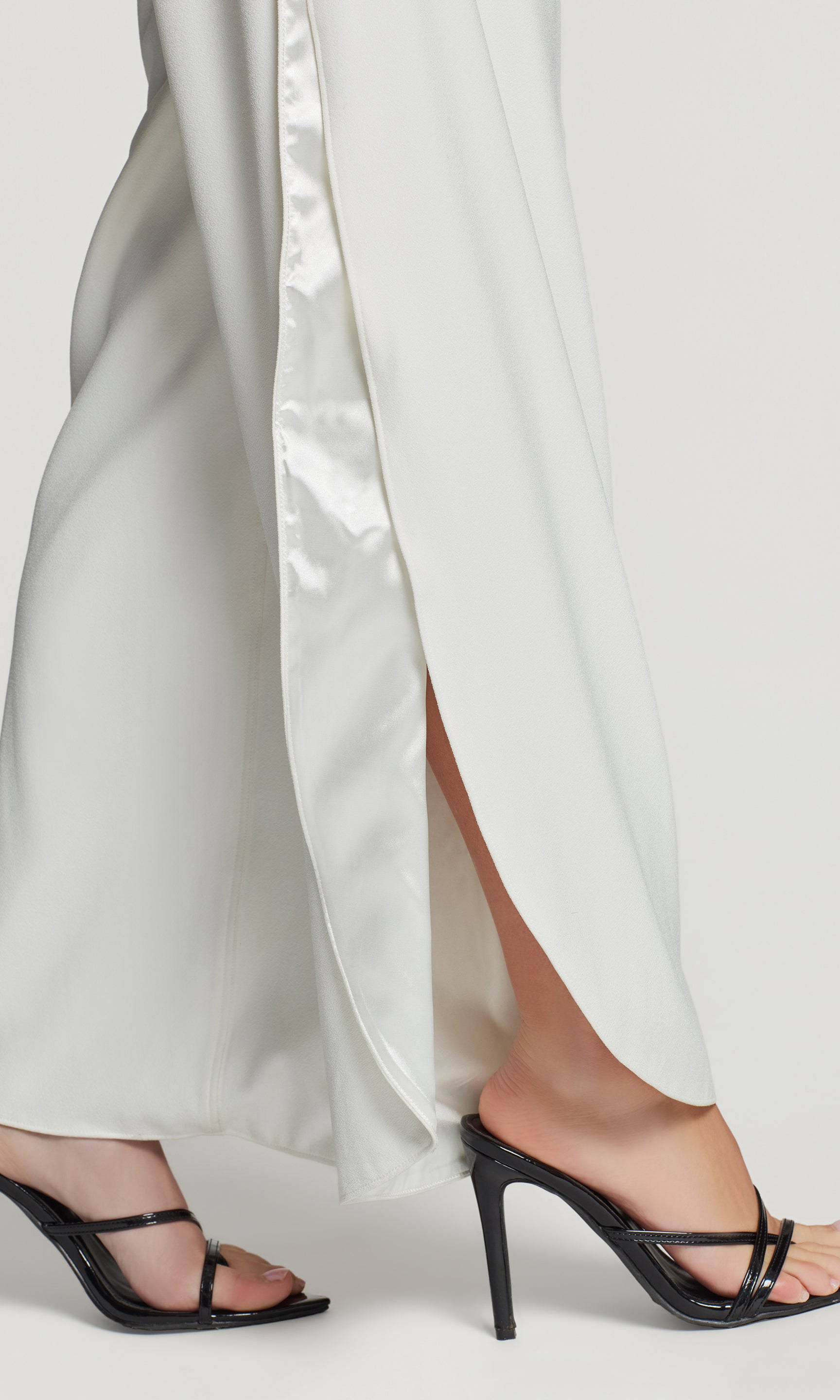 Close-up of white satin pants with a high slit and black high-heeled sandals on a white background