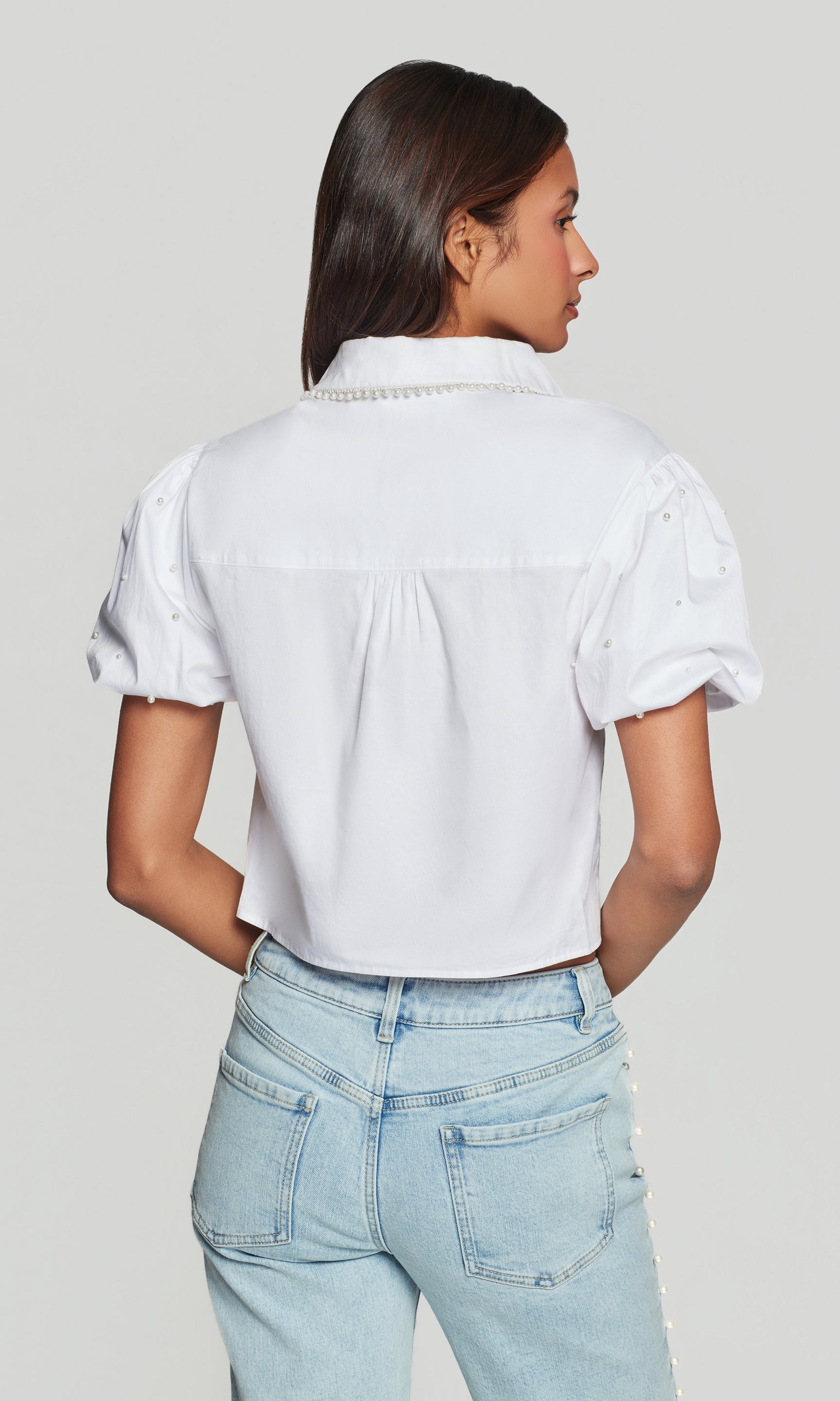 In a studio rear view, the model wears the Soo Pearl Poplin Shirt in white, highlighting the back yoke and relaxed, airy shape.