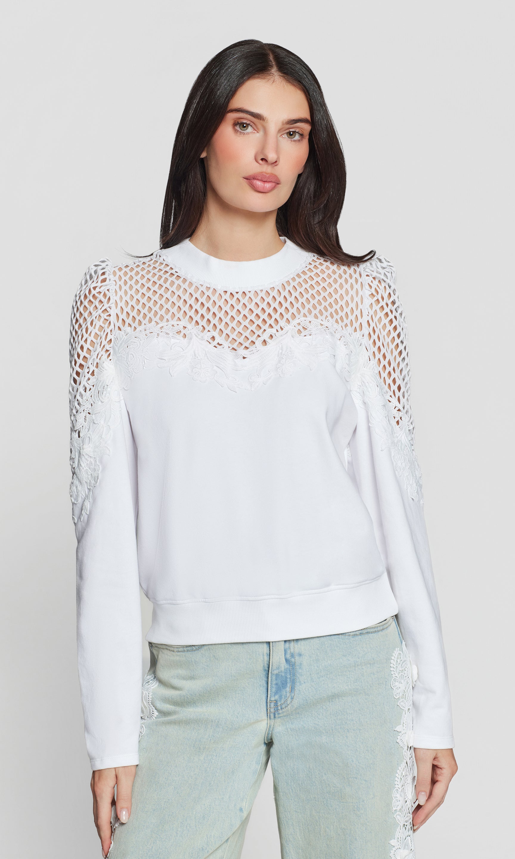 Woman wearing a white long-sleeve sweatshirt with mesh details on a plain background