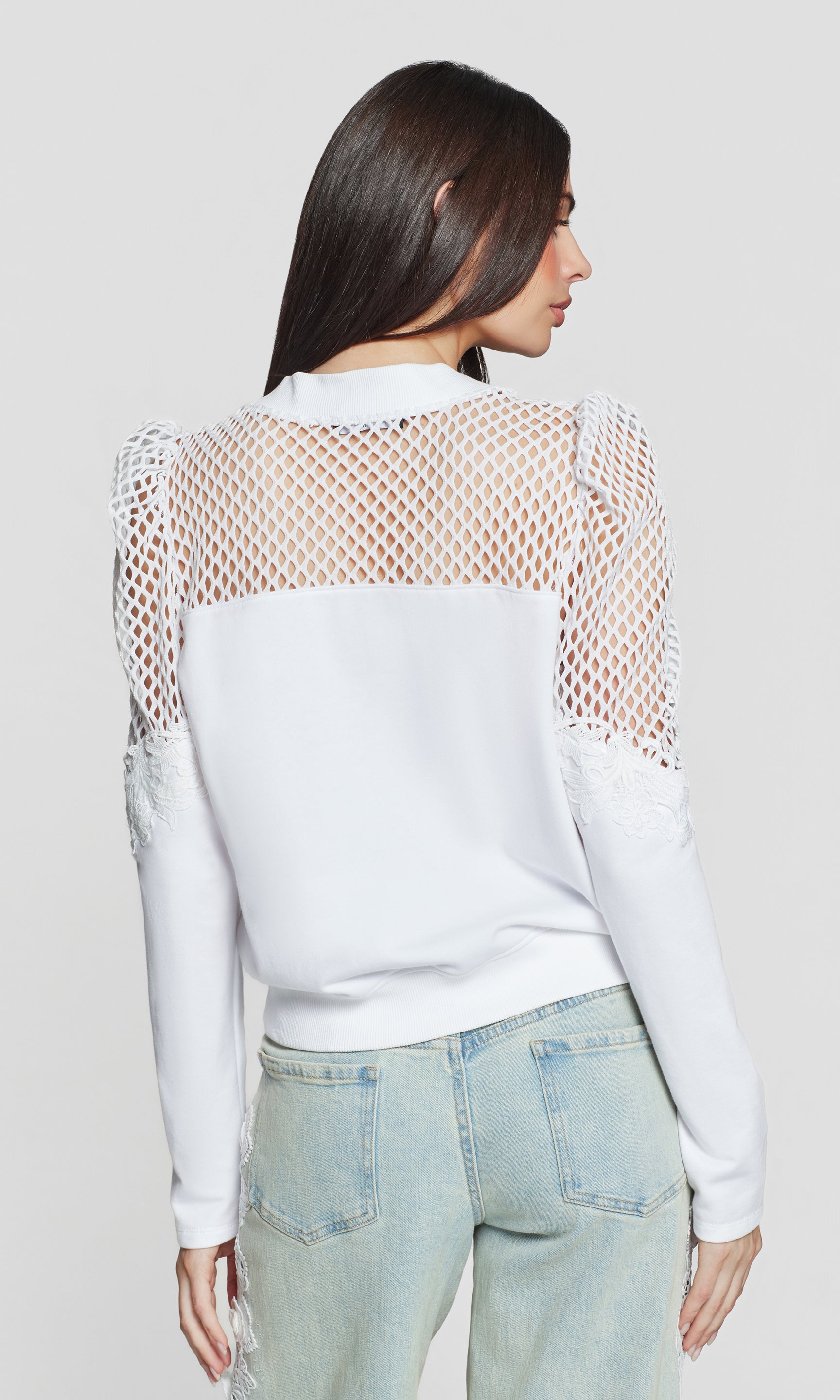 Back view of woman wearing a white long-sleeve sweatshirt with mesh details on a plain background