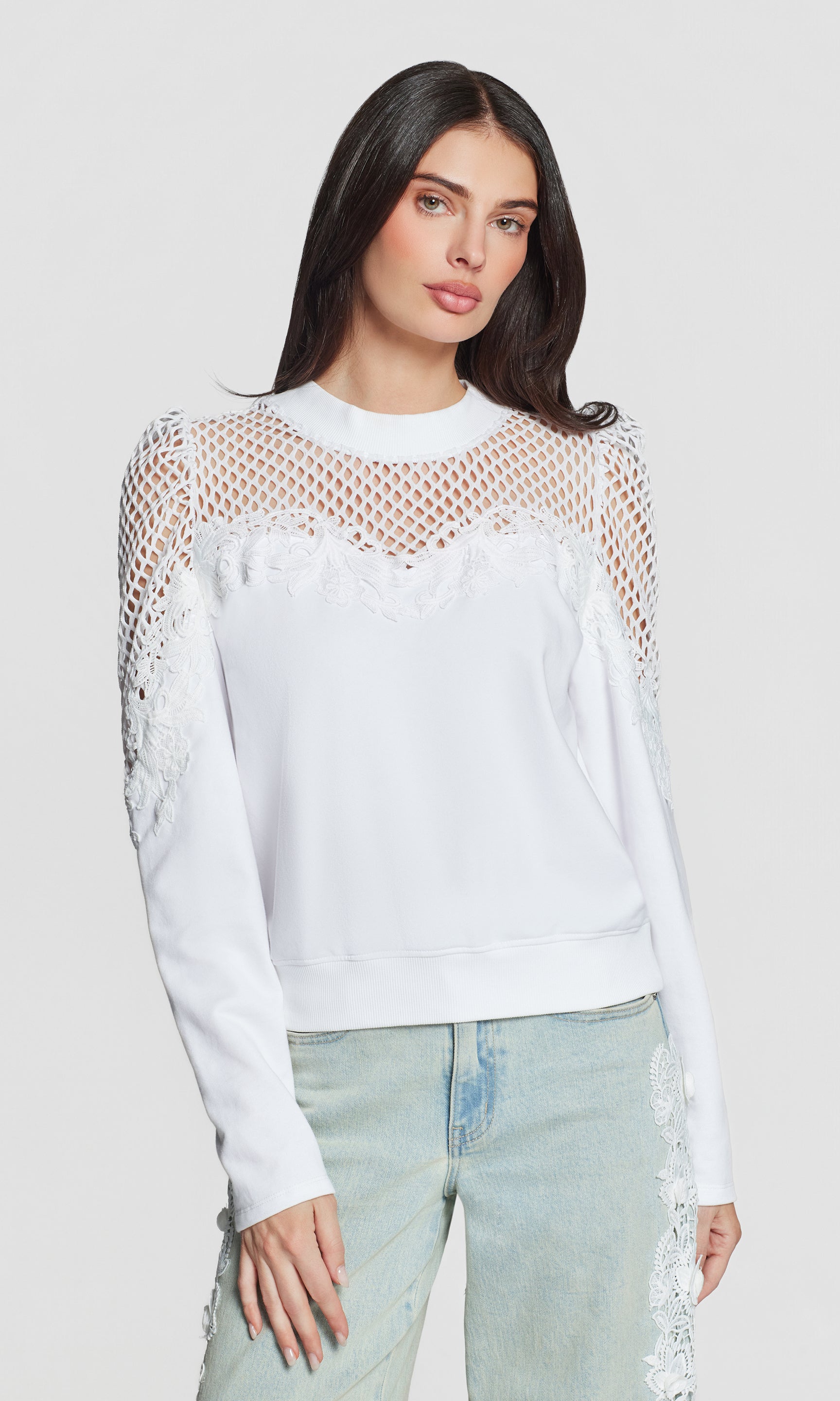 Woman wearing a white mesh sweatshirt with long sleeves on a plain background