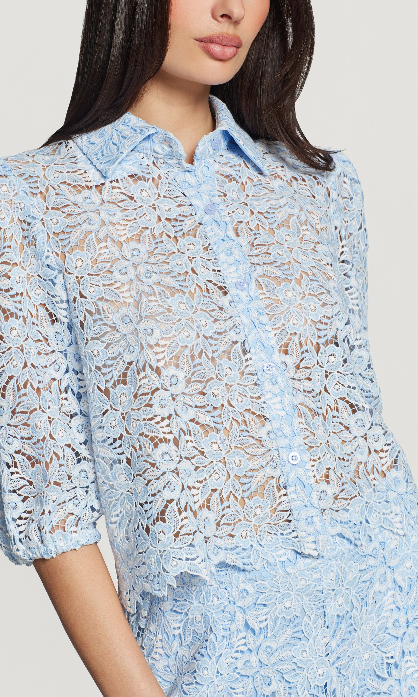 Close-up of light blue lace shirt worn by a model on a plain background