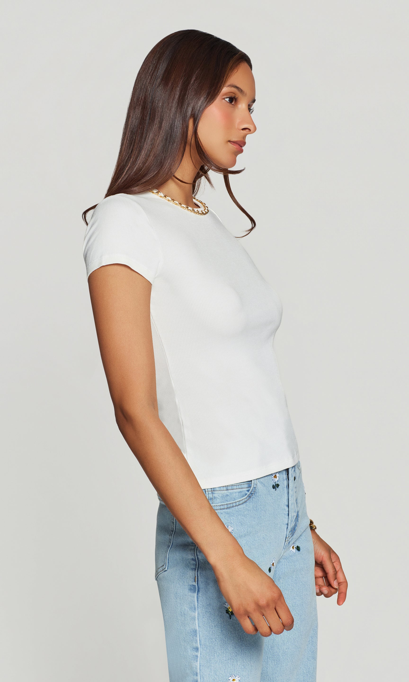 Side view of woman wearing a white t-shirt and light blue jeans on a plain background