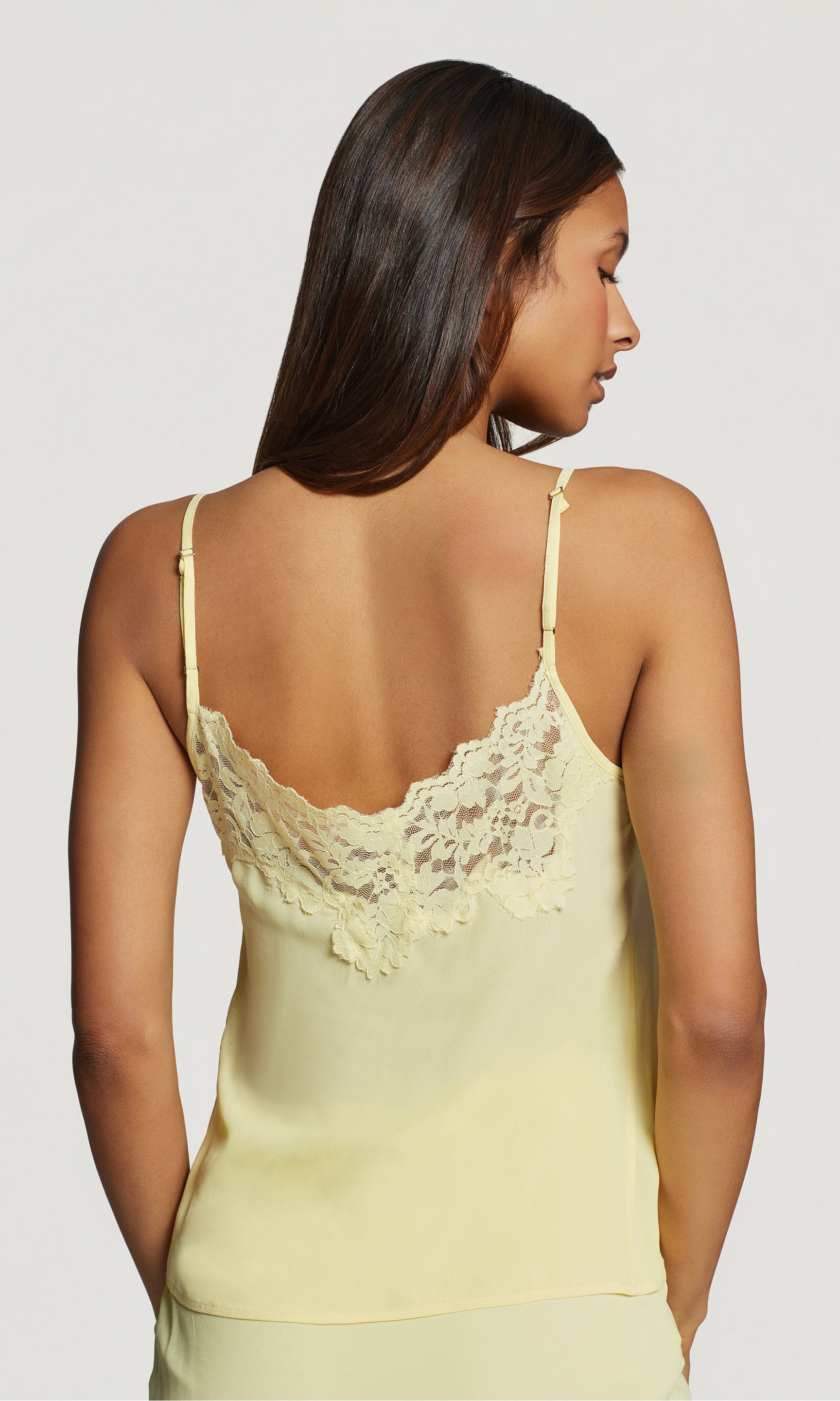 Back view of woman wearing a light yellow lace-trimmed camisole against a plain background