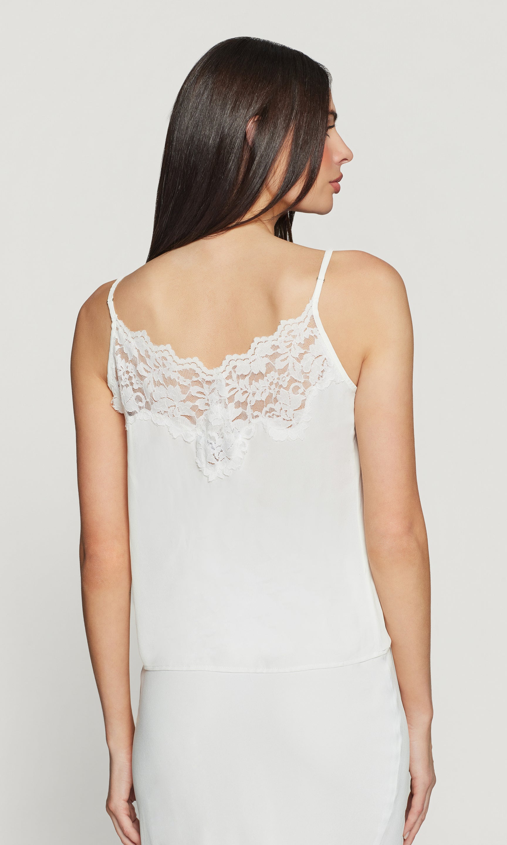 Back view of woman wearing a white lace-trimmed camisole against a plain background