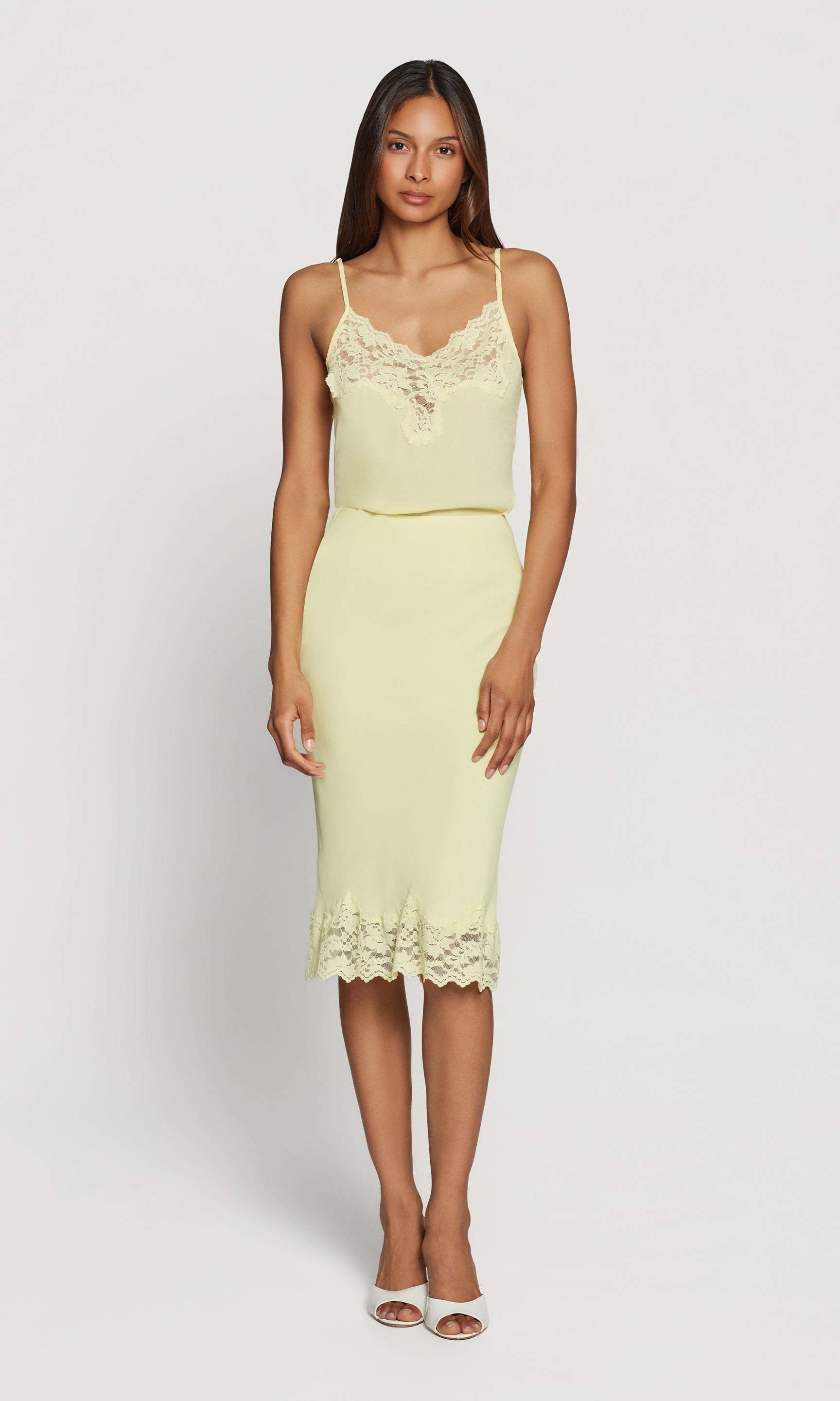 Woman wearing a light yellow top and matching skirt dress on a white background