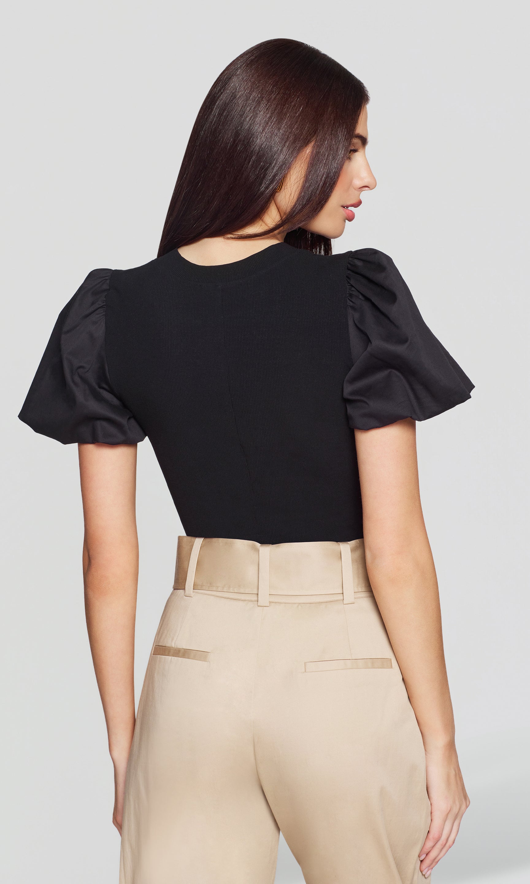 The model is shown in a rear view wearing the Teigan Poplin Combo Top in black, showcasing the crisp puff sleeves and clean back silhouette.