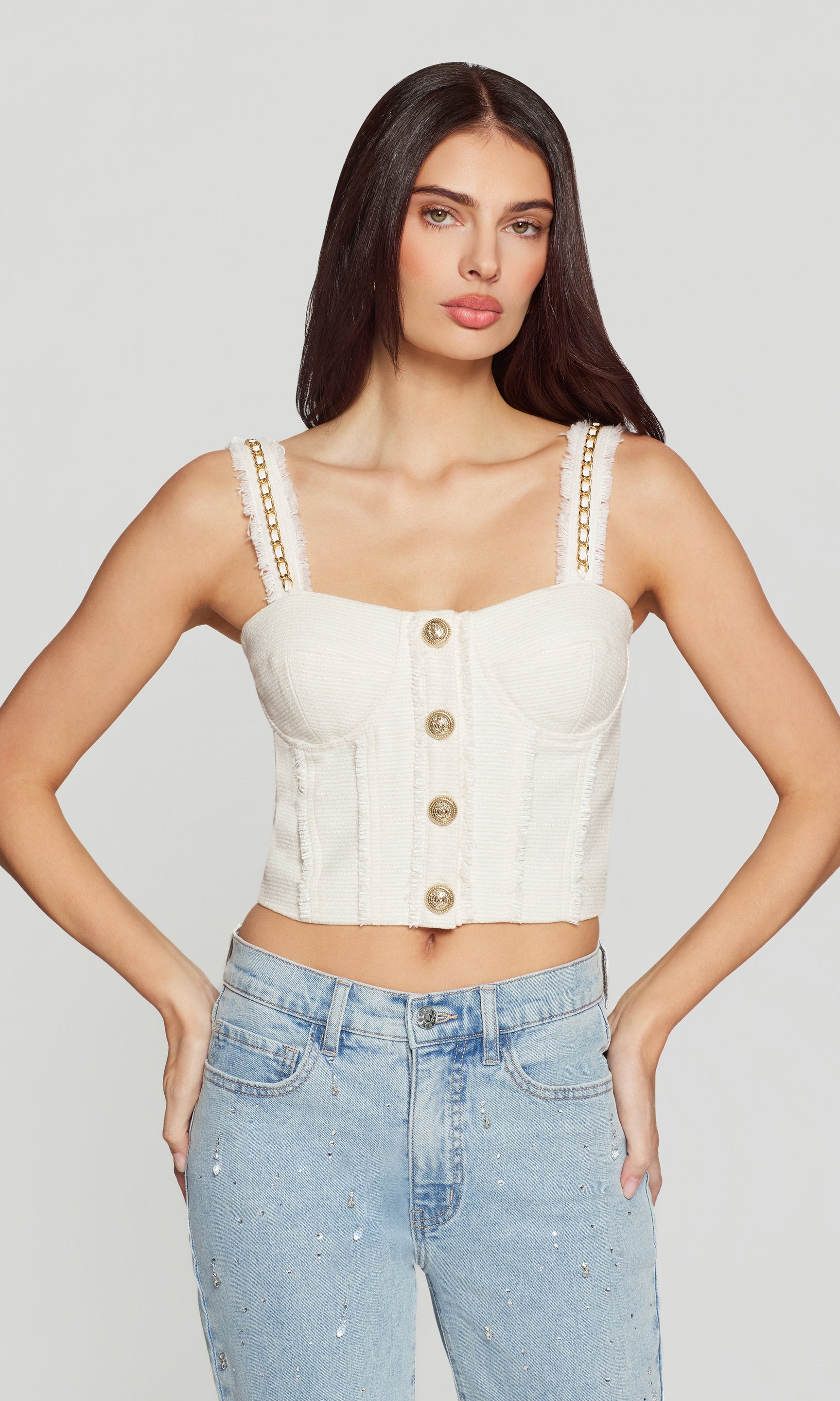 Woman wearing a white chain-strap top and blue jeans on a plain background