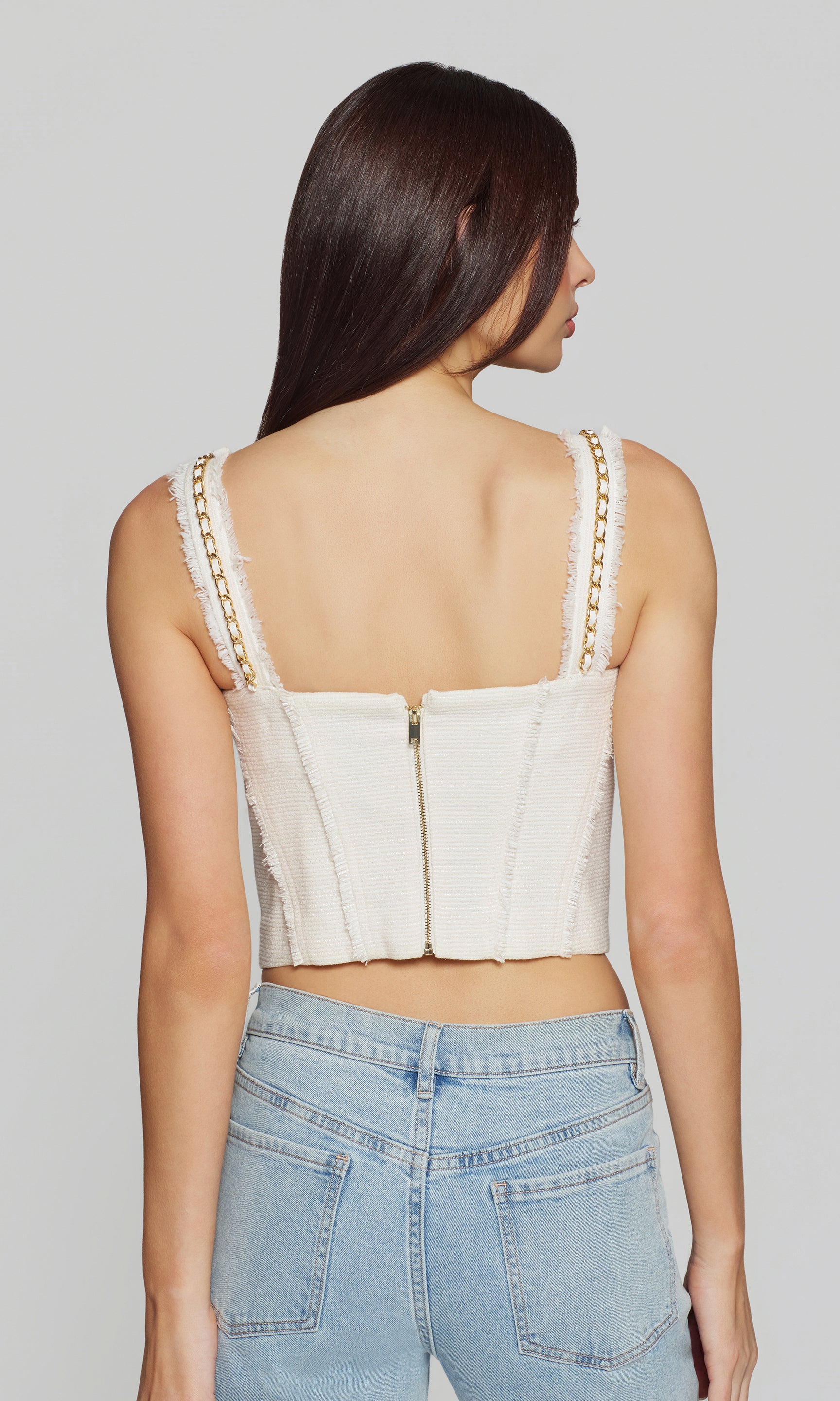 Back view of woman wearing a white crop top with lace details and blue jeans on a plain background