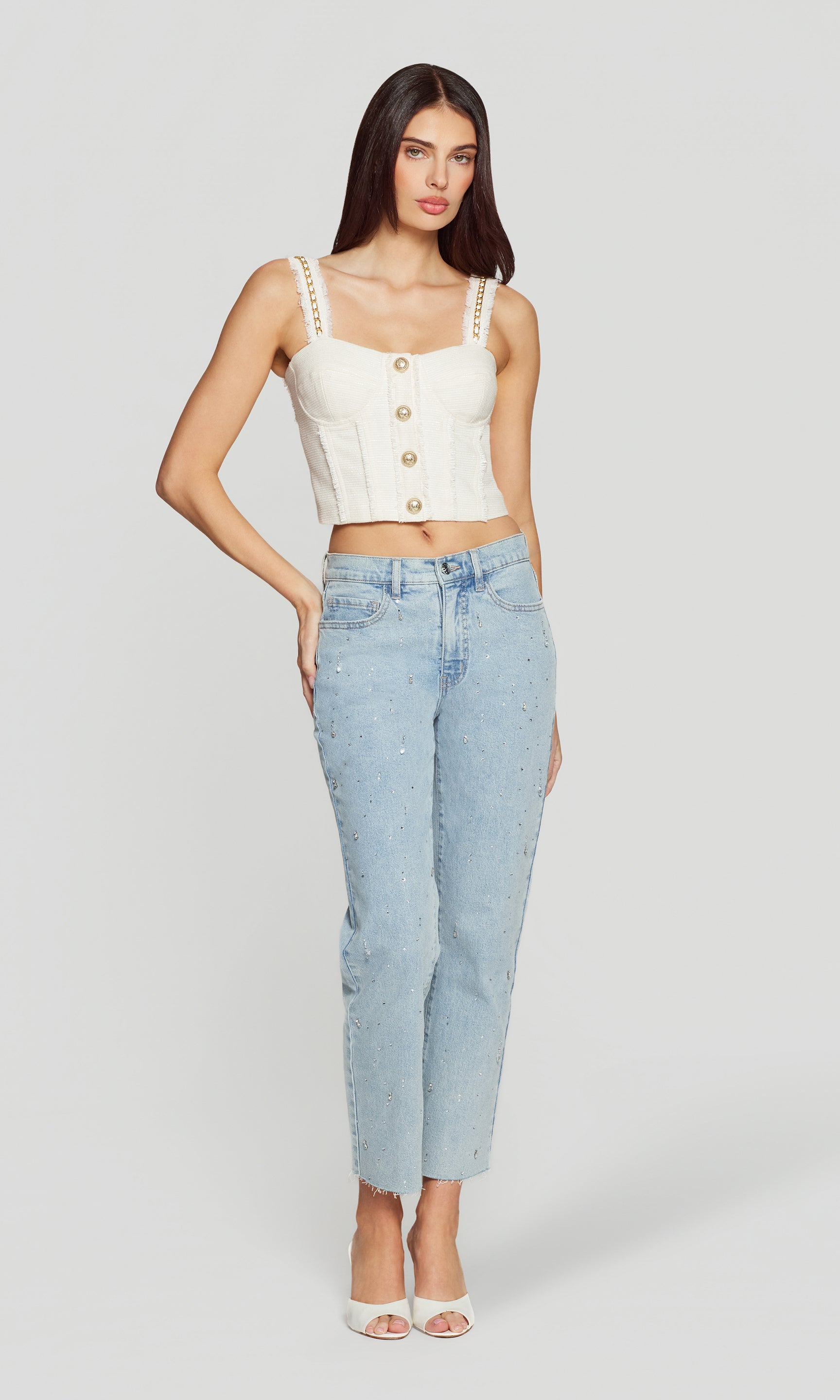 Woman wearing a white sleeveless top with buttons and light blue jeans on a white background