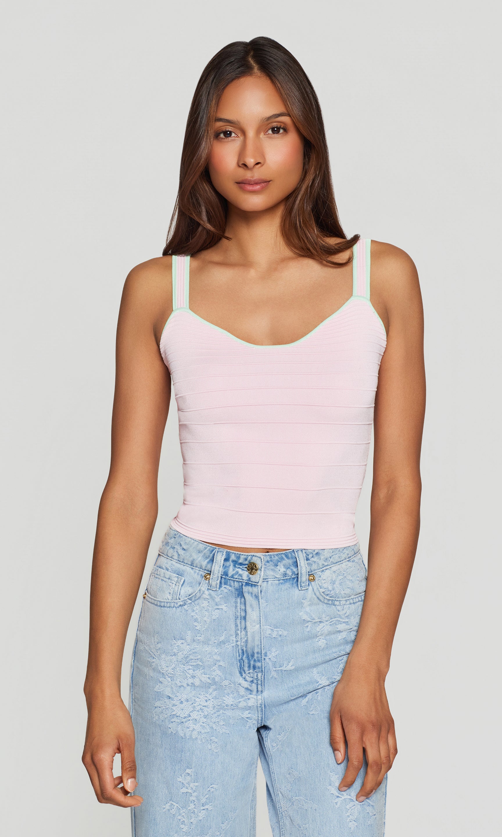 Woman wearing a light pink tank top and light blue jeans against a plain background