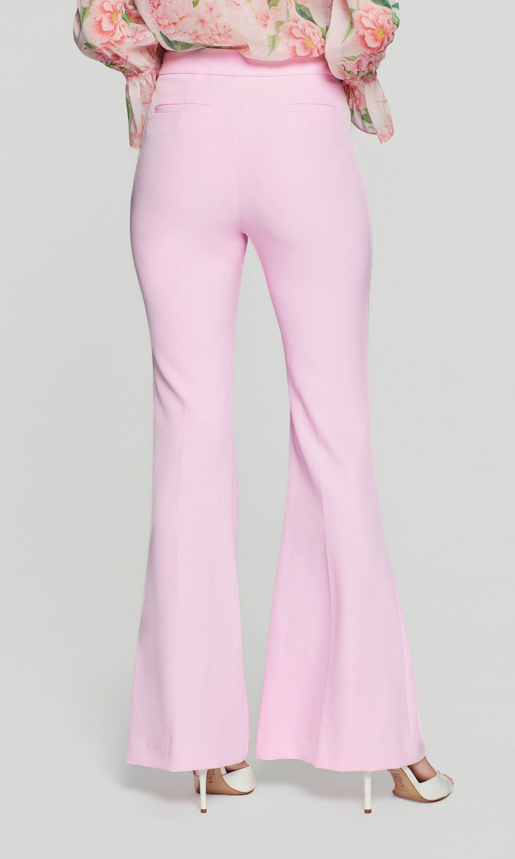 Back view of pink flared pants worn with a floral blouse on a light gray background