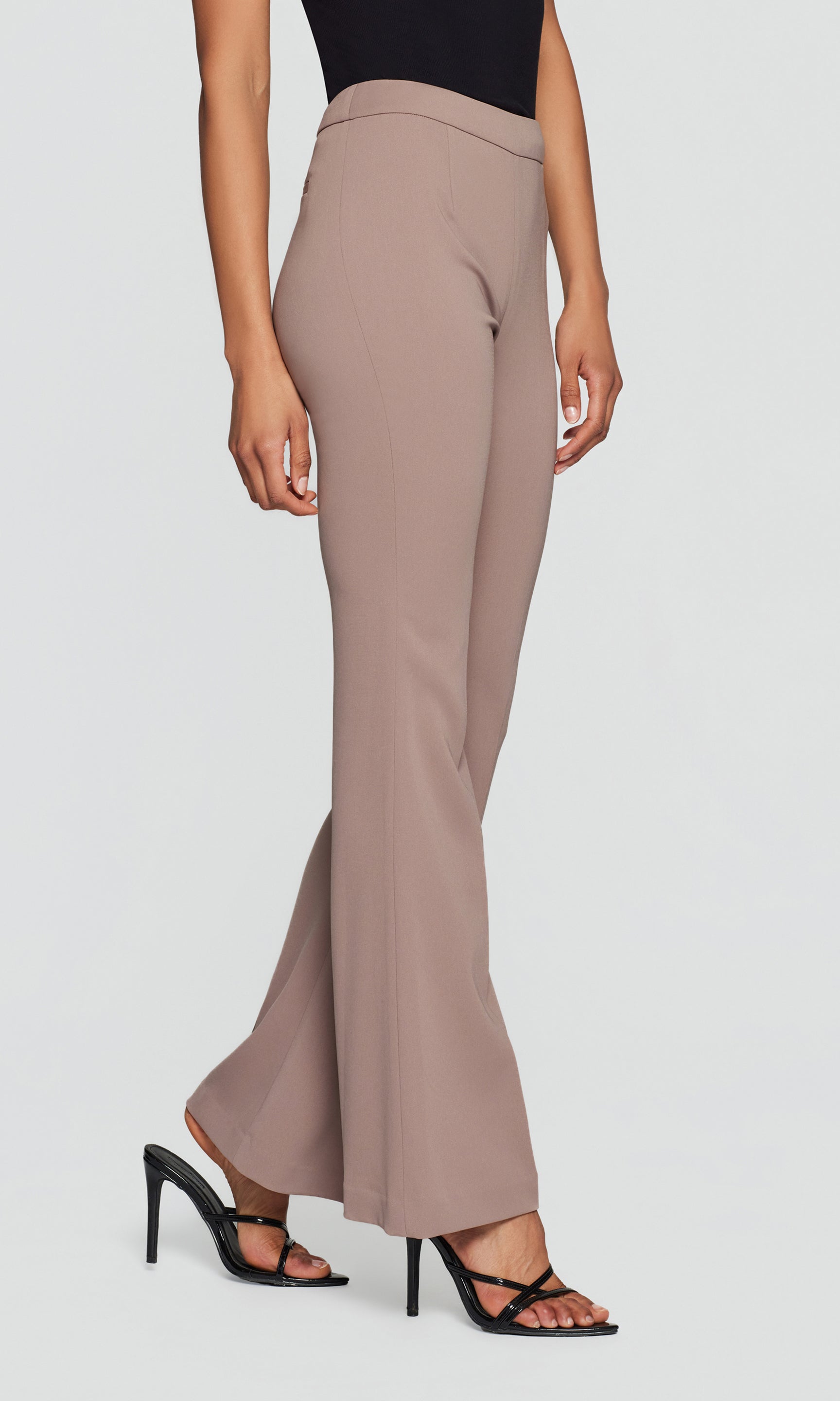 Side view of a person wearing beige pants with a black top and heels.