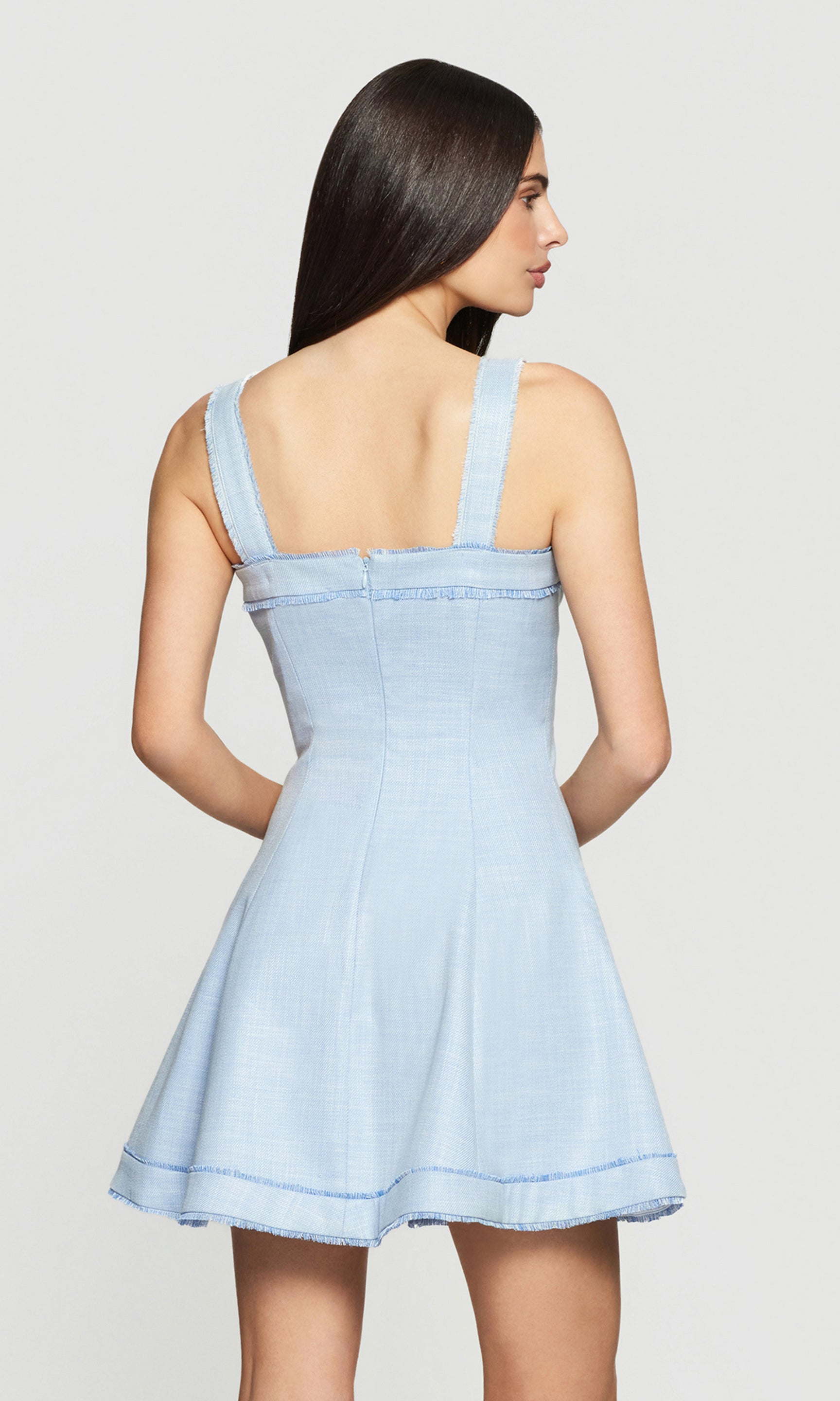 Model wears a chambray blue button-front mini dress in a full body rear view, showing the strap back and flared hem.