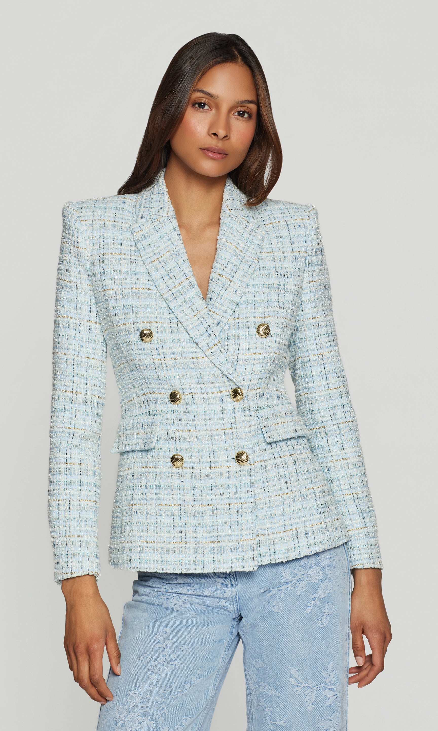 Woman wearing a light blue plaid blazer with gold buttons on a plain background