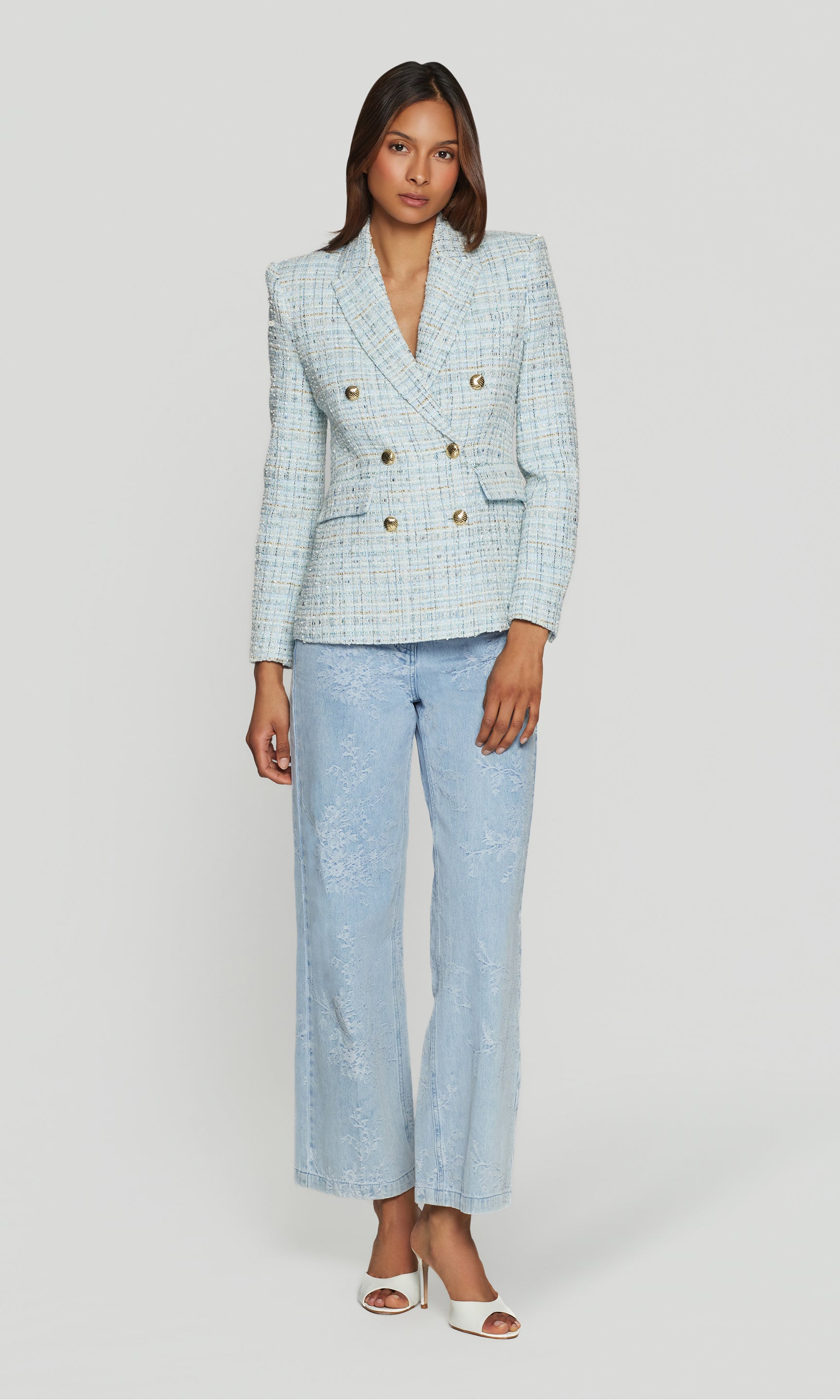Woman wearing a light blue tweed checkered blazer with blue jeans on a white background