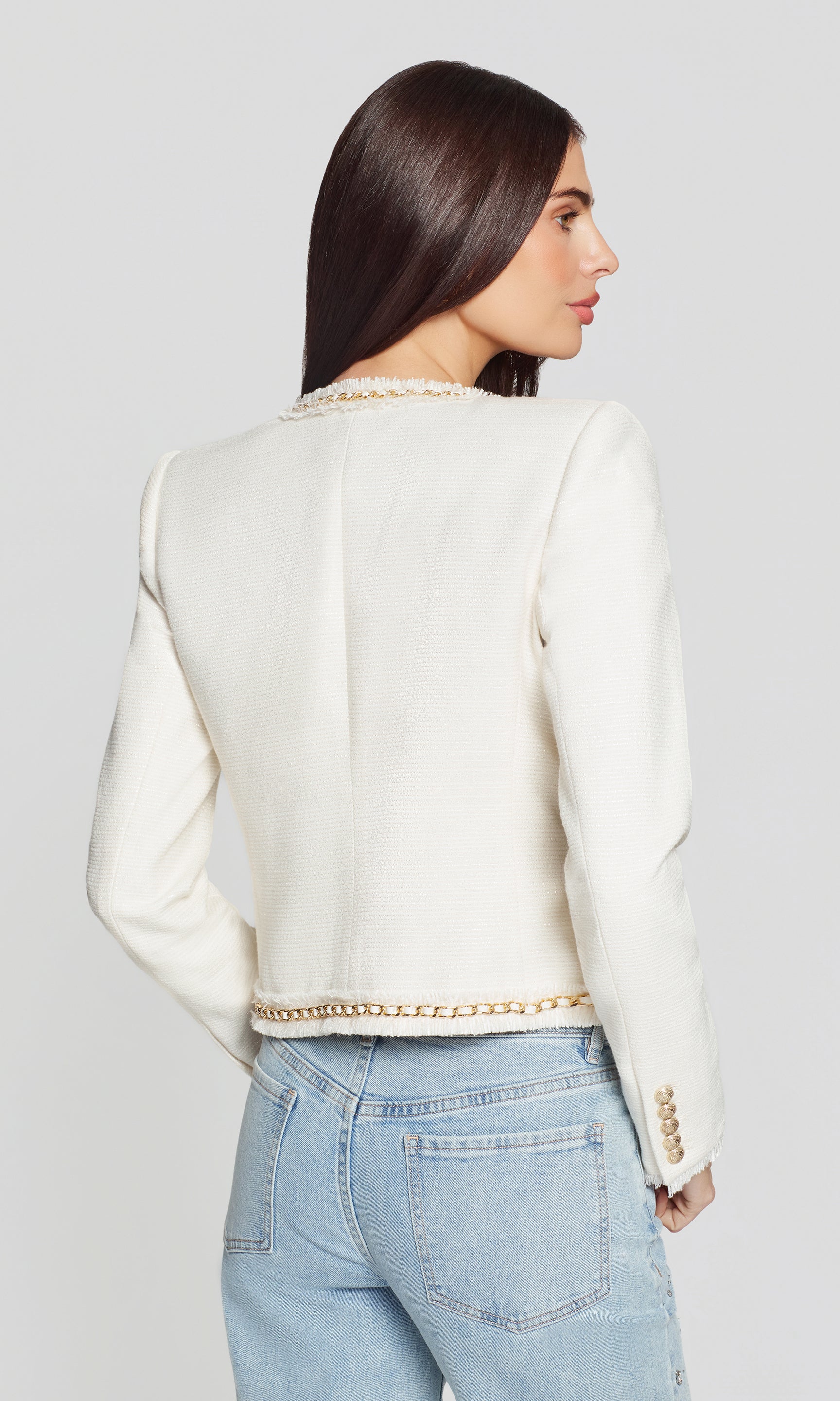 Back view of woman wearing a white jacket with gold trim on a plain background