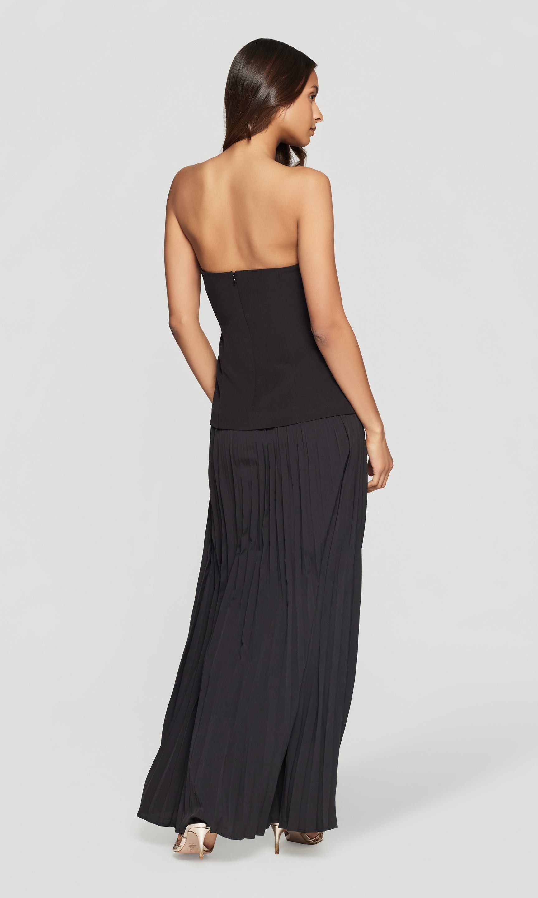 Back view of woman wearing a black strapless dress on a white background