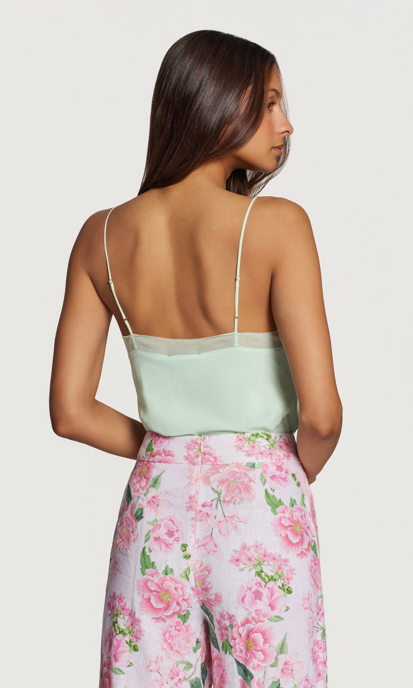 Back view of woman wearing a light green top and pink floral pants on a white background
