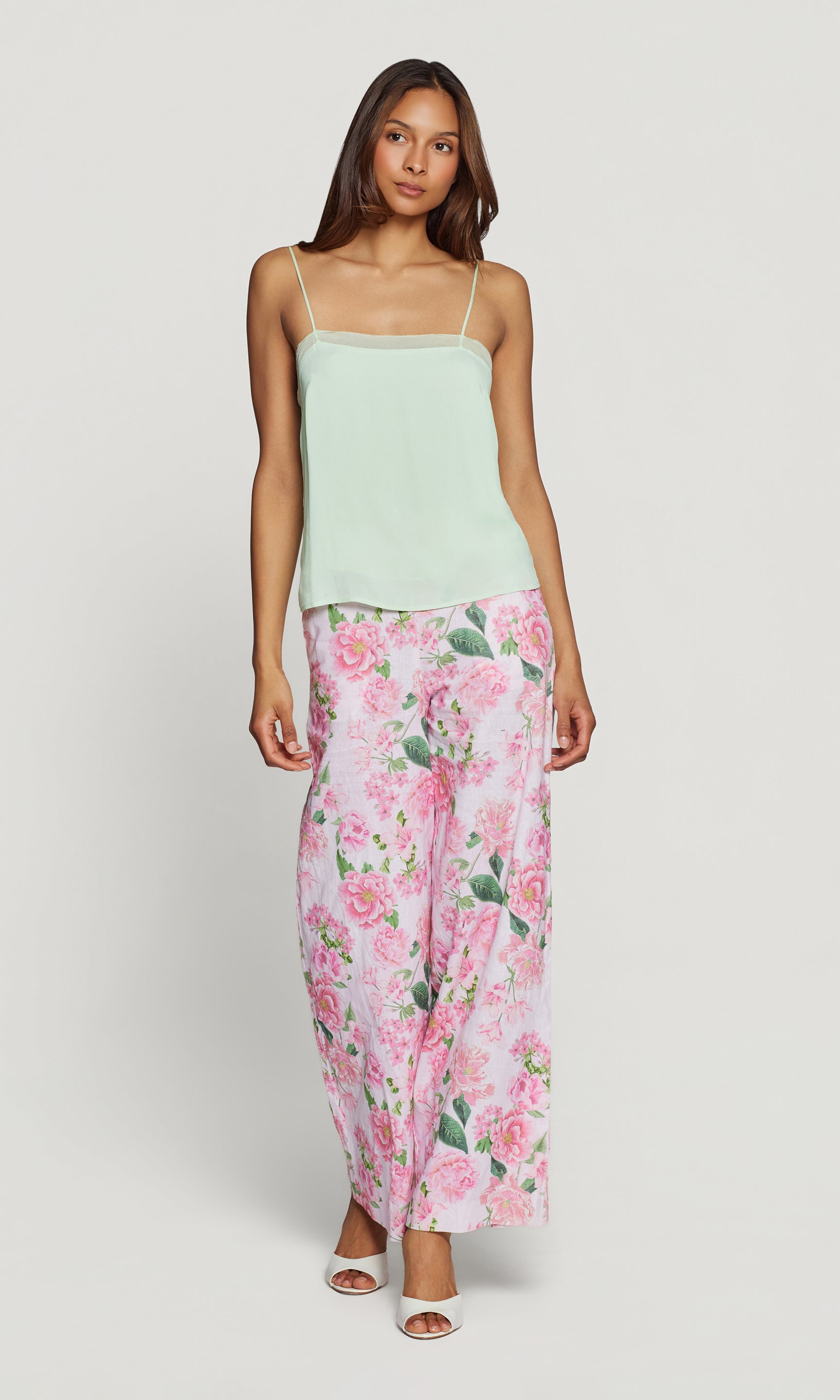 Woman wearing a light green top and floral pants on a white background