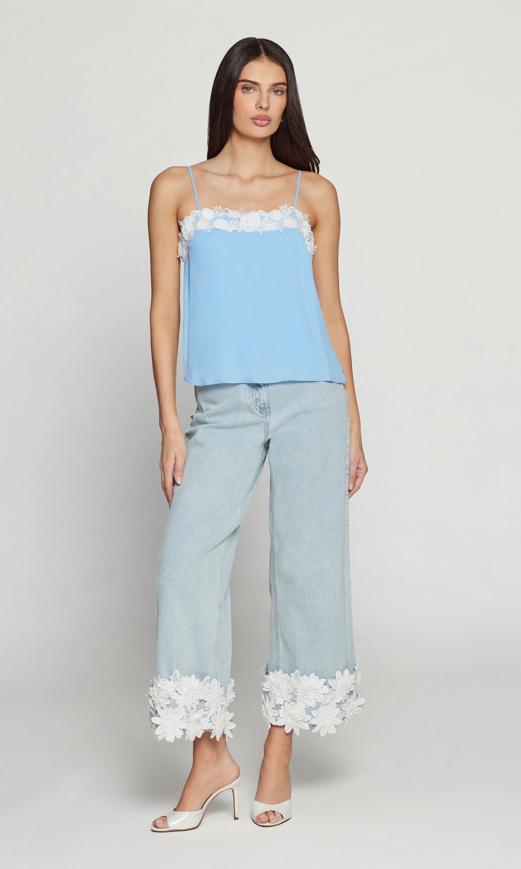 Woman wearing a light blue top and pants with white lace details on a white background