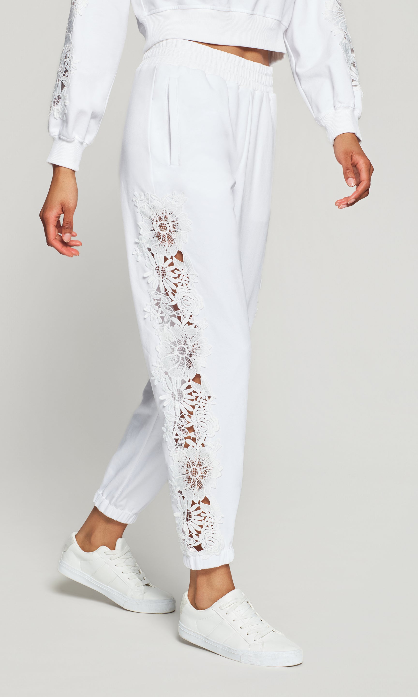 White outfit with lace detailing on pants against a plain background