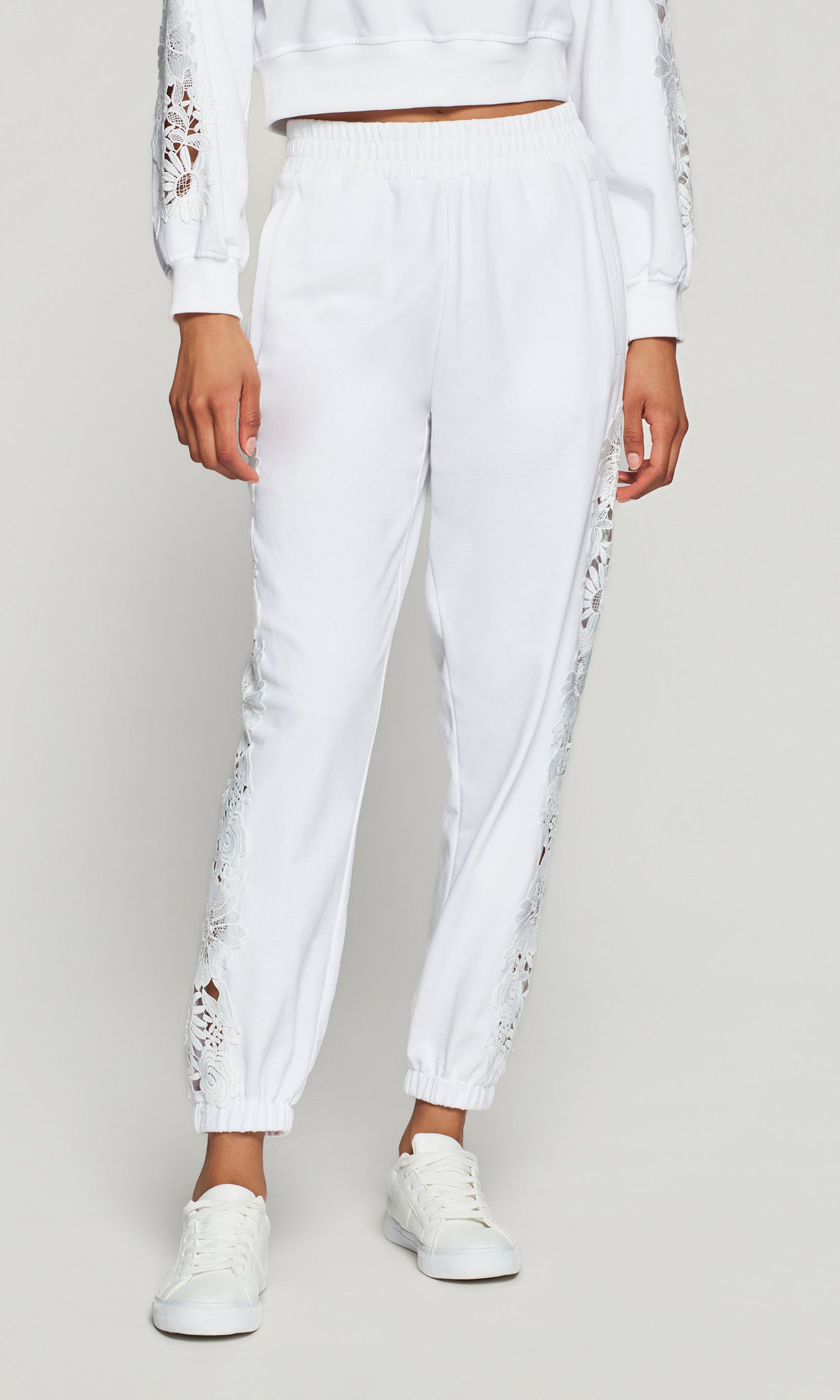 White jogger pants with lace details on a plain background