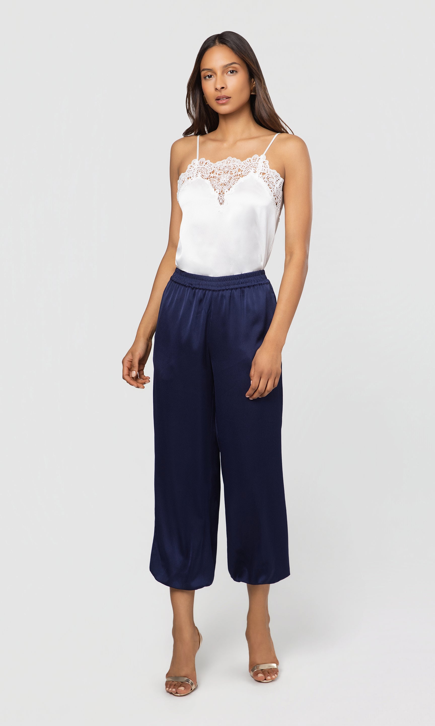 Woman wearing a white lace top and navy wide-leg pants on a light gray background
