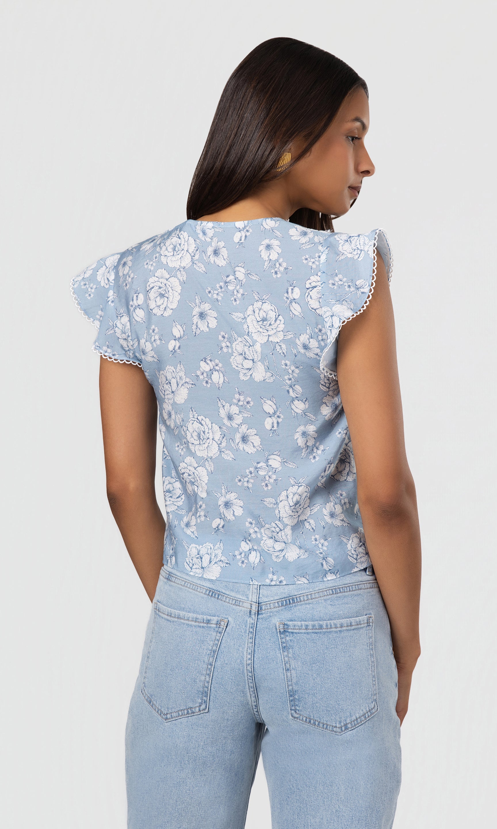 Back view of woman wearing a light blue floral top and jeans on a white background