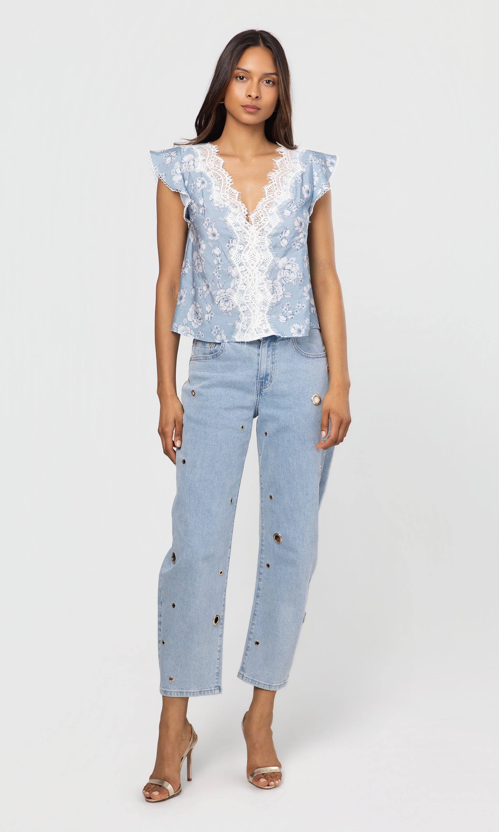 Woman wearing a light blue floral top and jeans on a white background