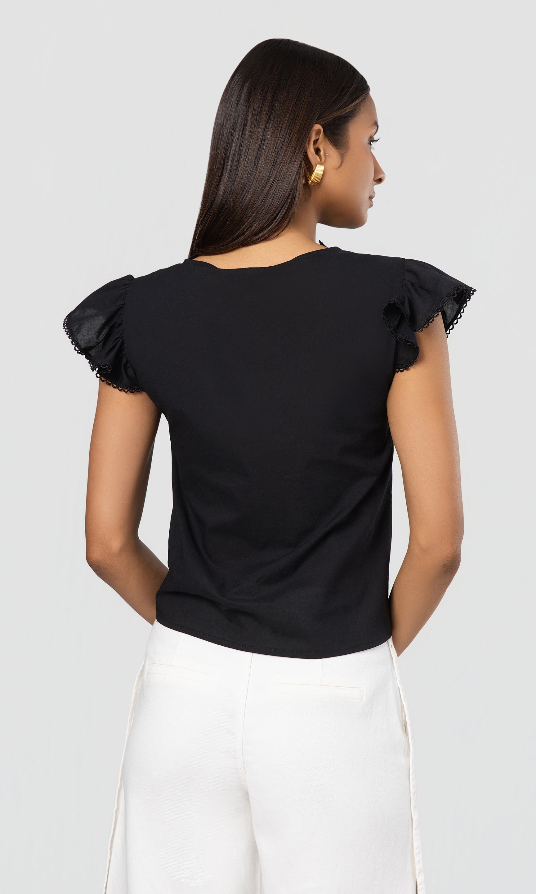 Back view of woman wearing a black top with ruffled sleeves on a white background