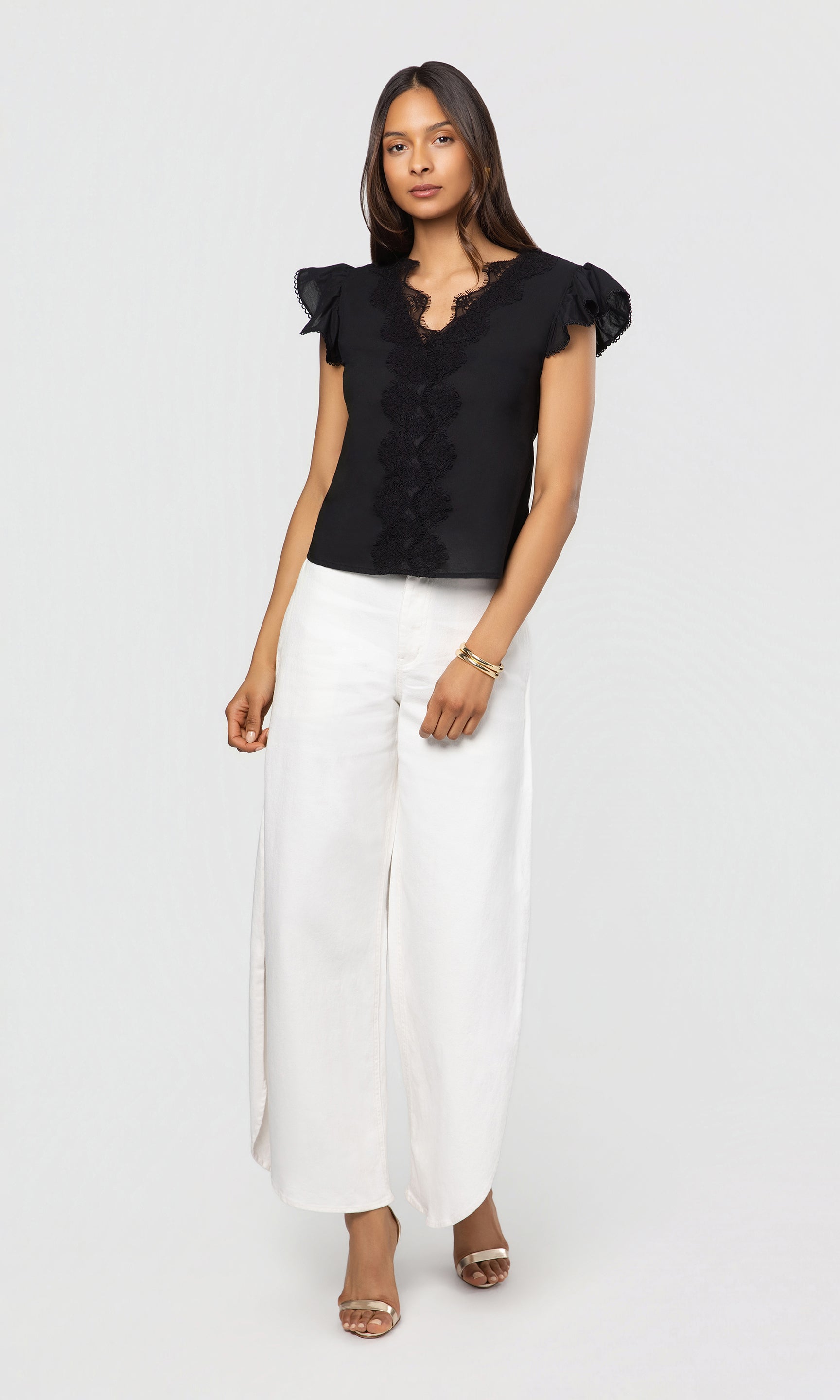 Woman wearing a black blouse with ruffled sleeves and white pants on a white background