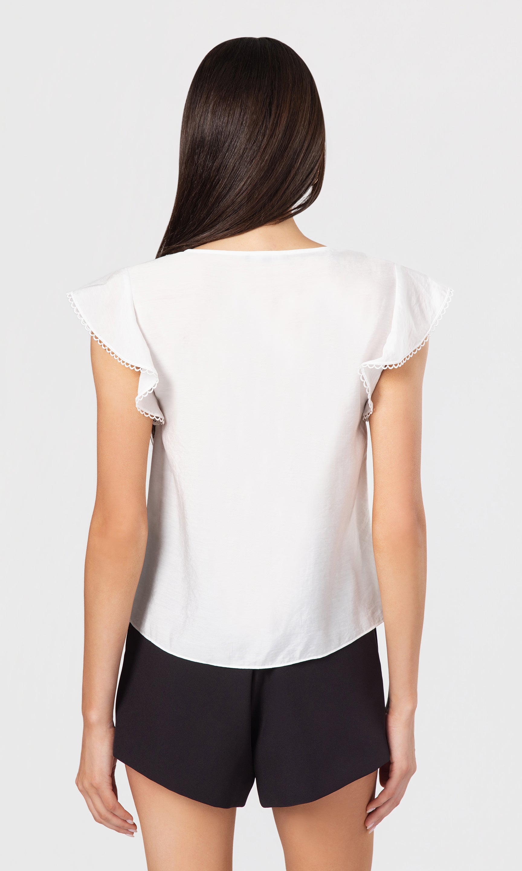 Back view of woman wearing a white blouse with lace trim on a plain background