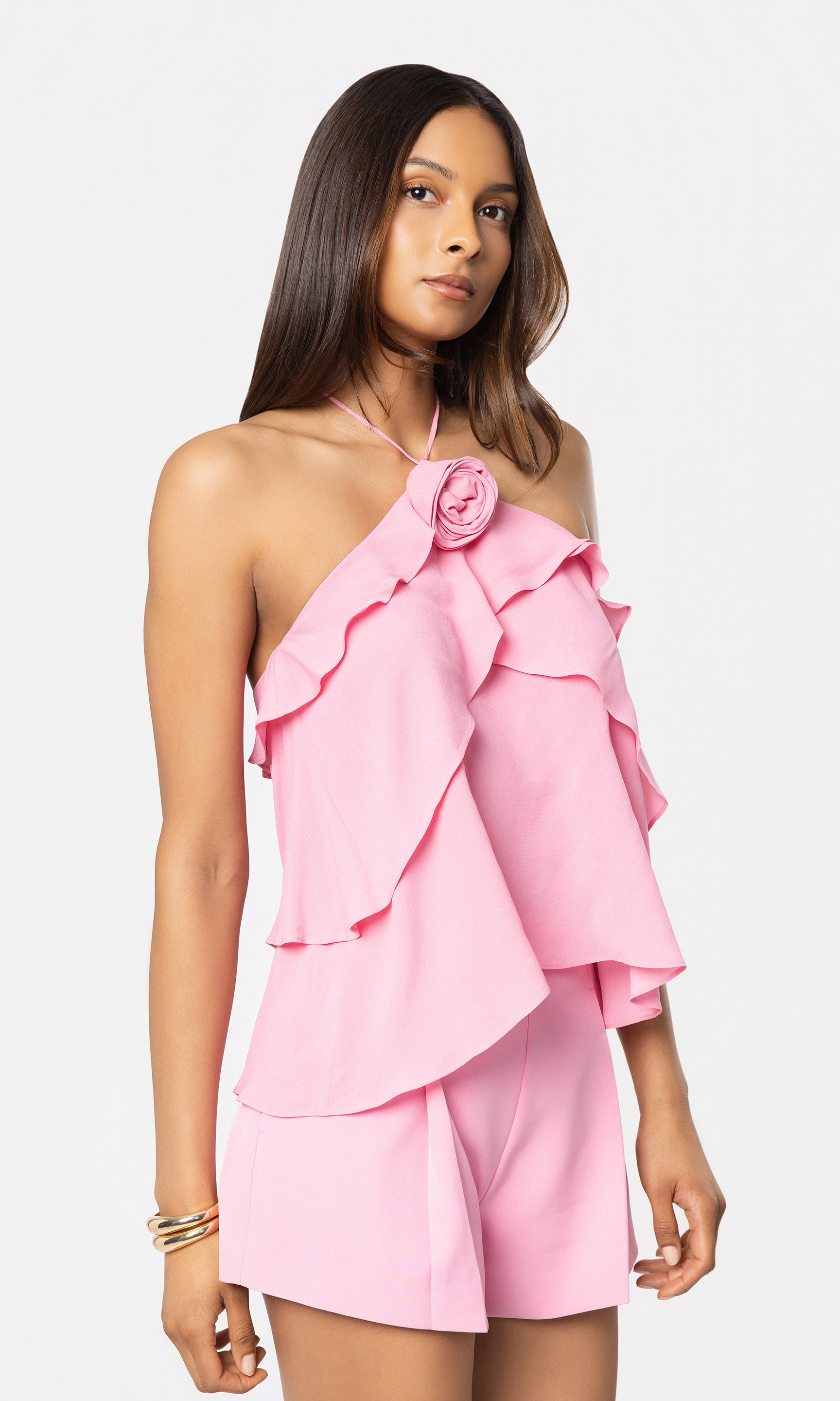 Side view of woman wearing a pink ruffled top and shorts on a white background