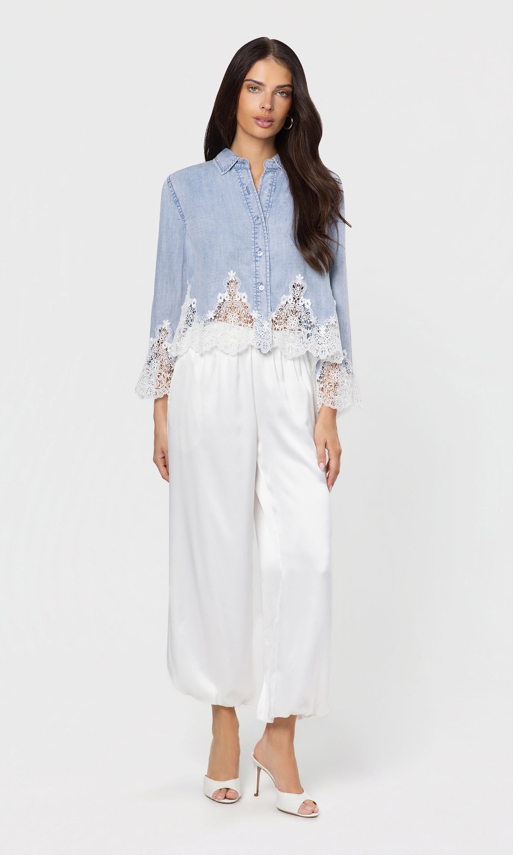 Woman wearing a light blue shirt with lace details and white pants on a white background
