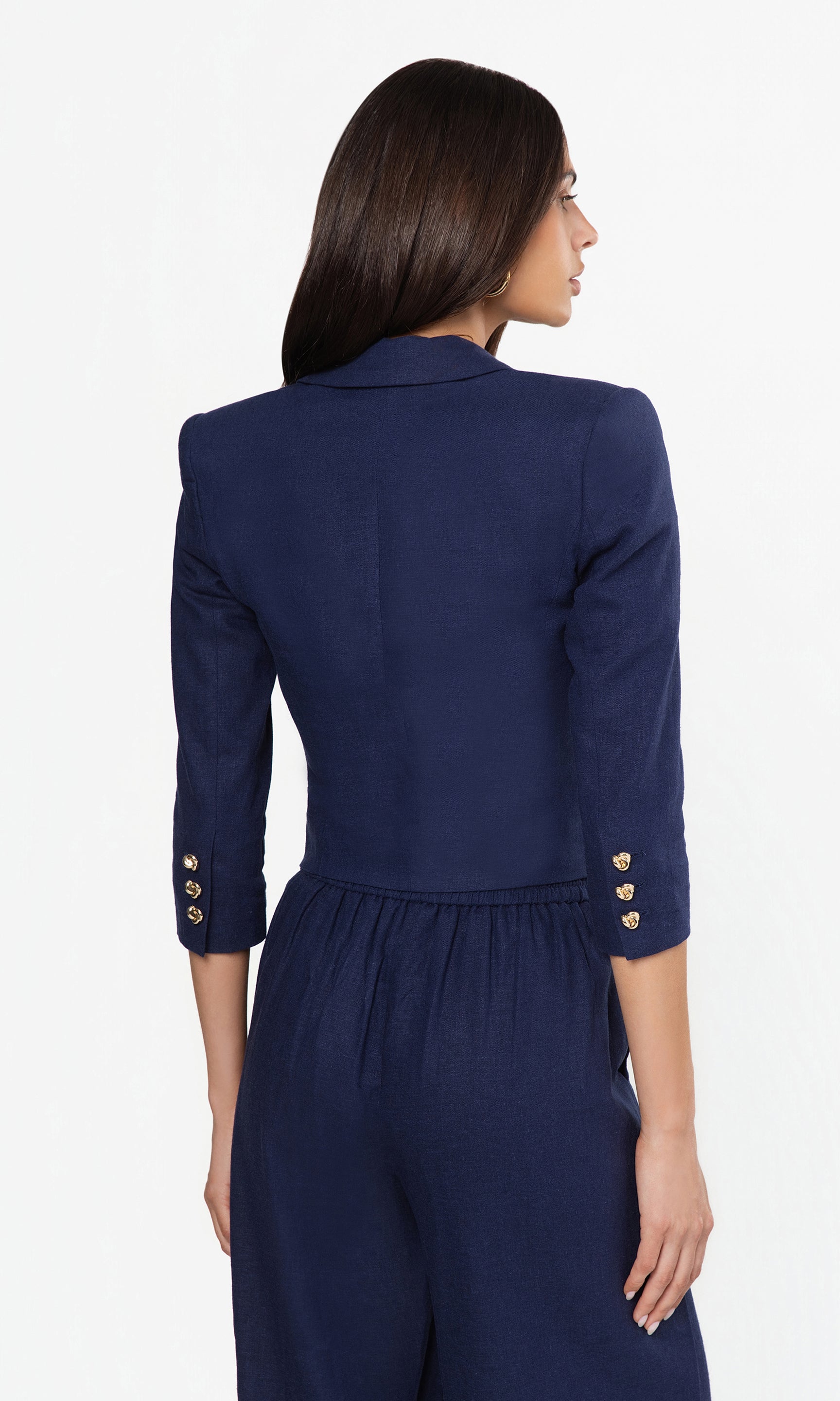 Back view of woman wearing a navy blue outfit with gold buttons on a white background