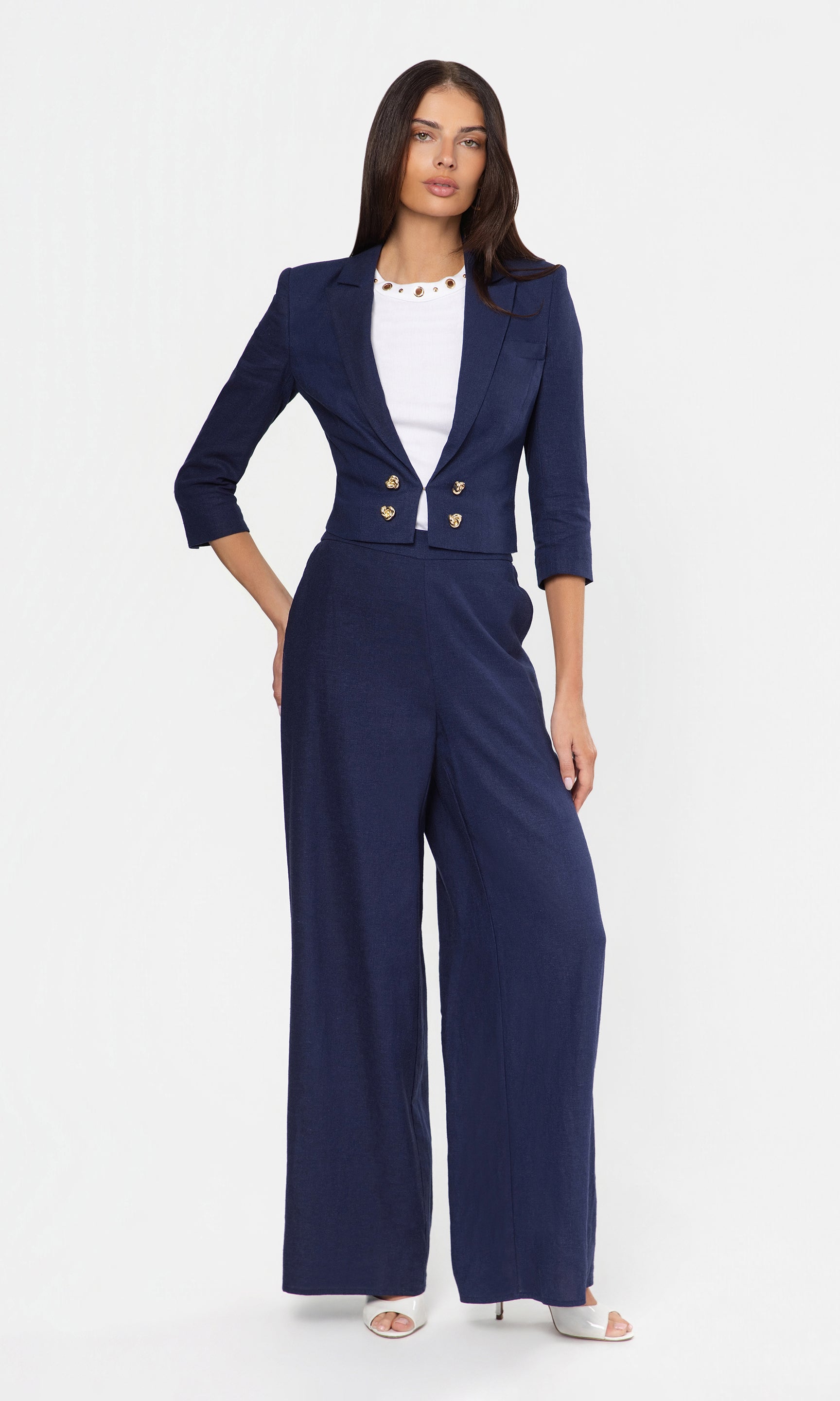 Woman wearing a navy blue linen suit with gold buttons on a white background