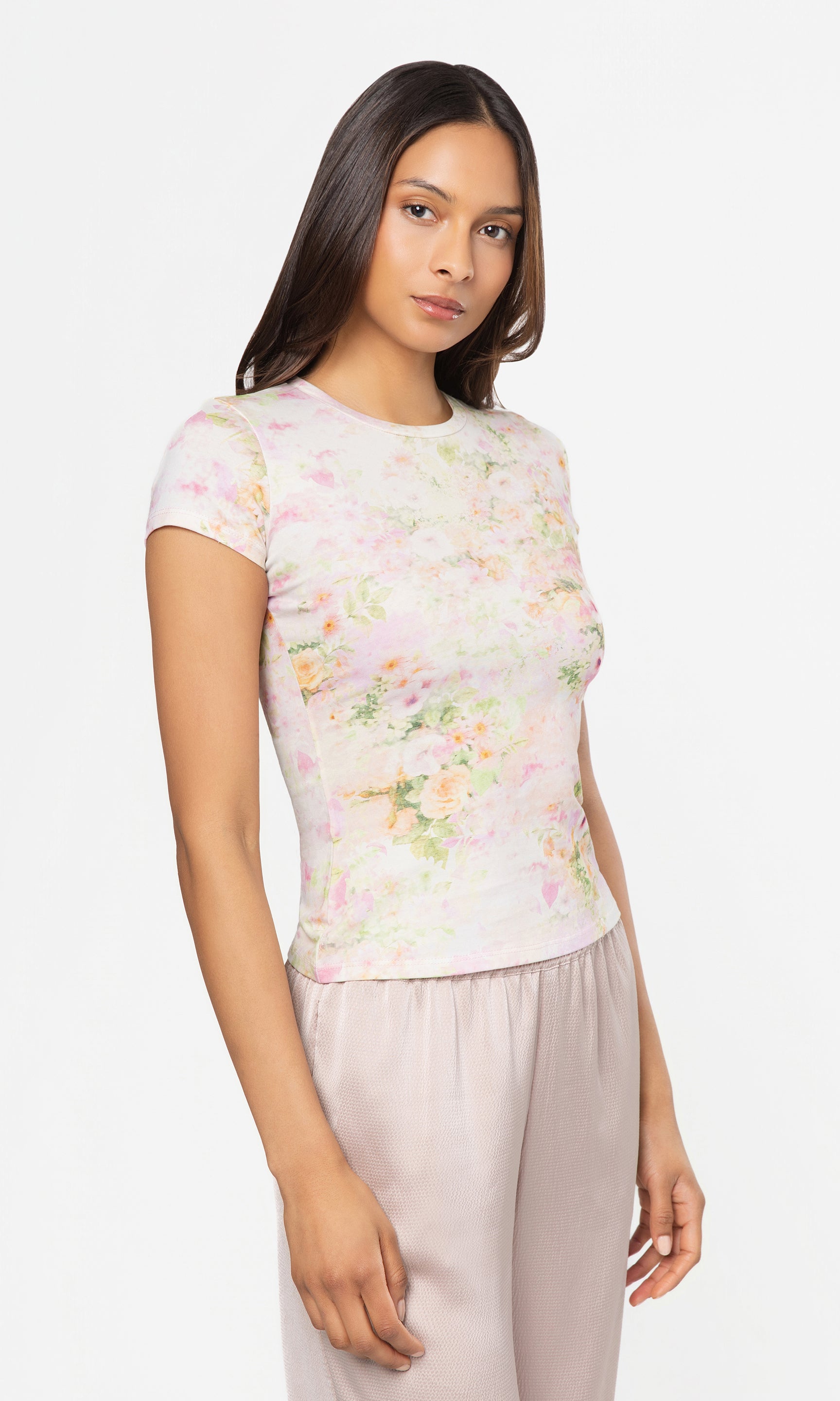 Side view of woman wearing a floral top and light pants on a white background