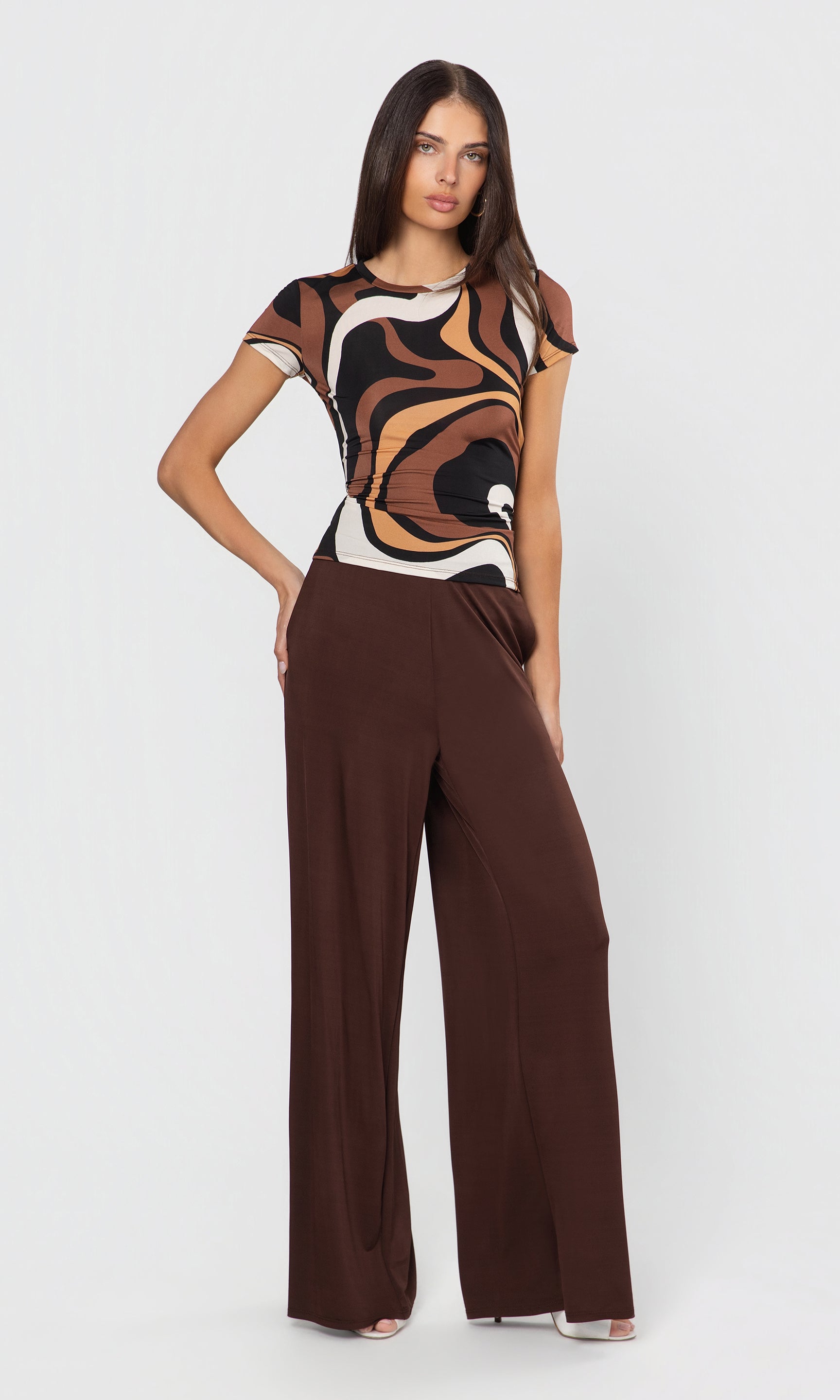 Woman wearing a patterned top and brown wide-leg pants on a white background