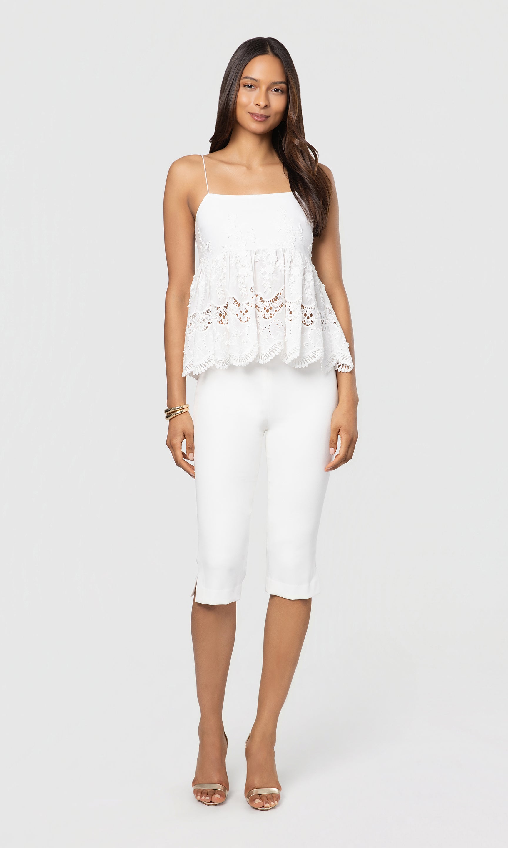 Woman wearing a white lace top with floral details and white pants on a white background