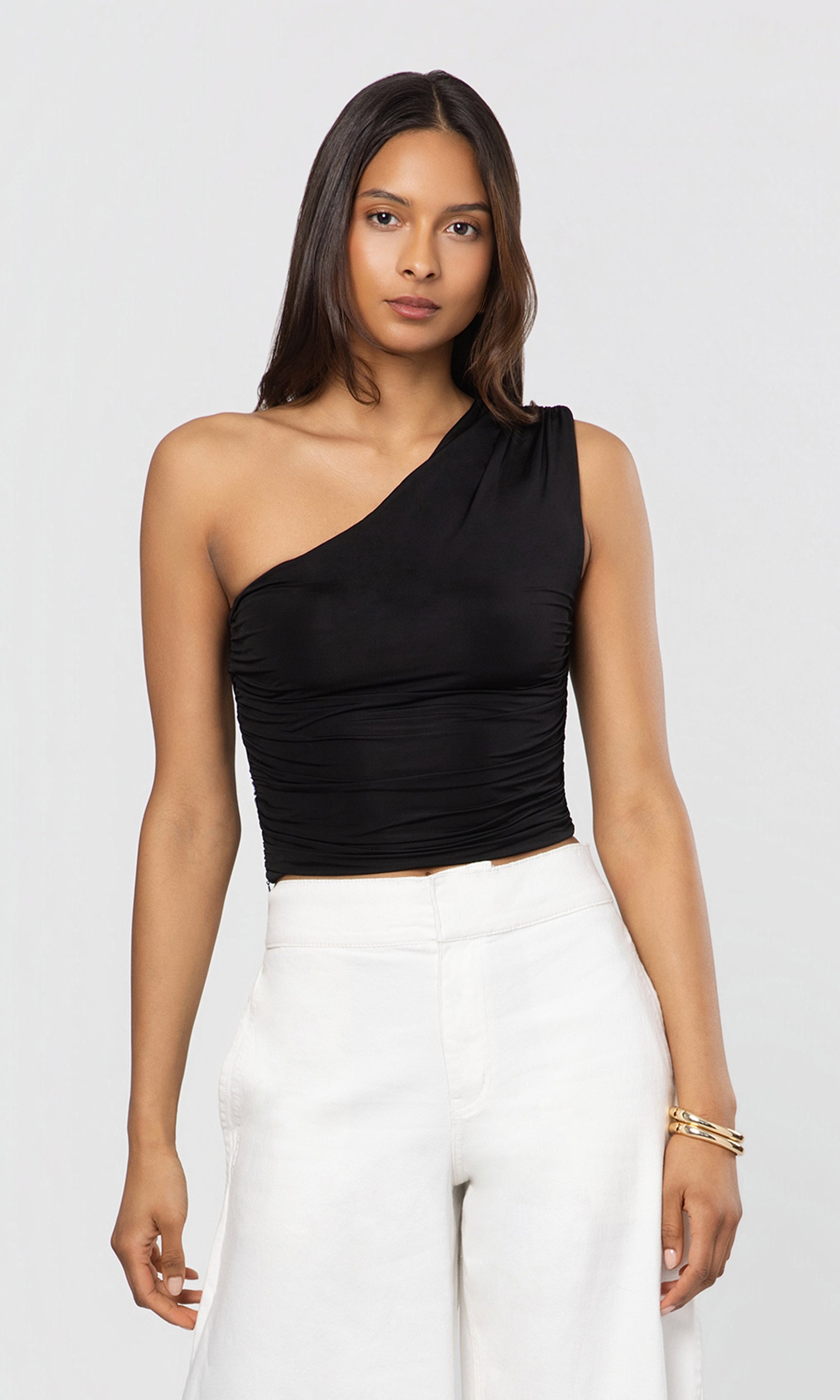 Woman wearing a black one-shoulder top and white pants on a light gray background