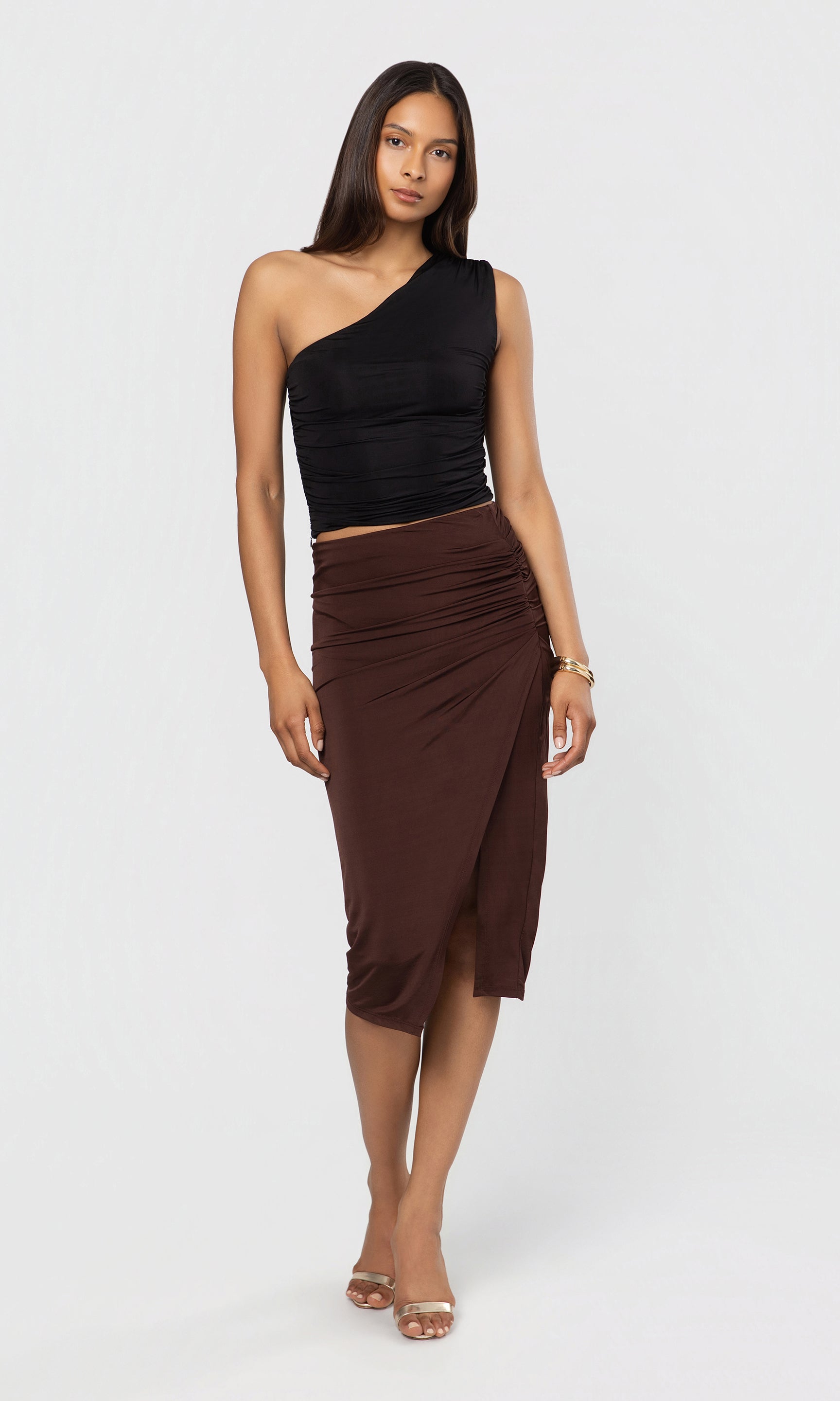 Woman wearing a black one-shoulder top and brown skirt on a white background
