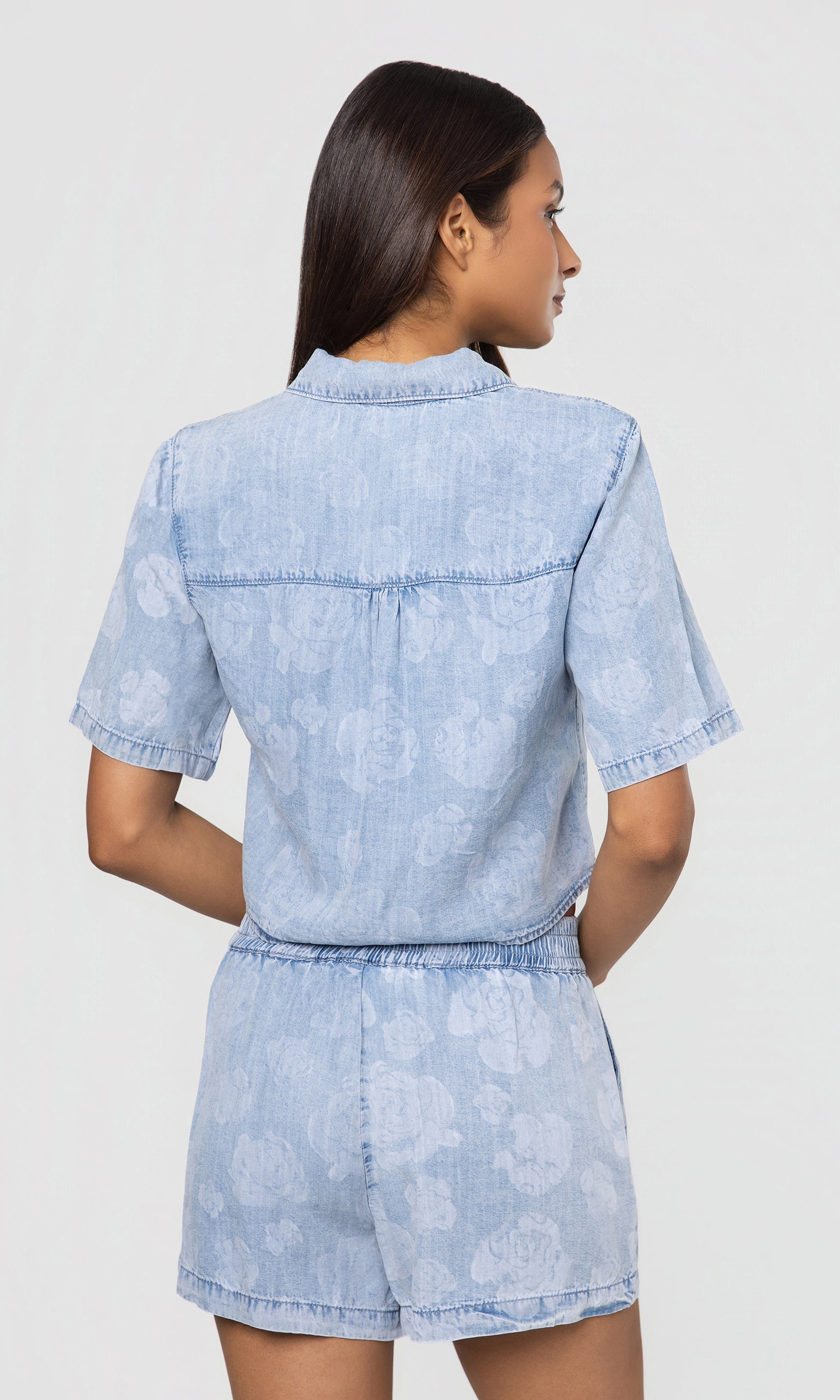 Back view of woman wearing a light blue matching top and shorts on a white background