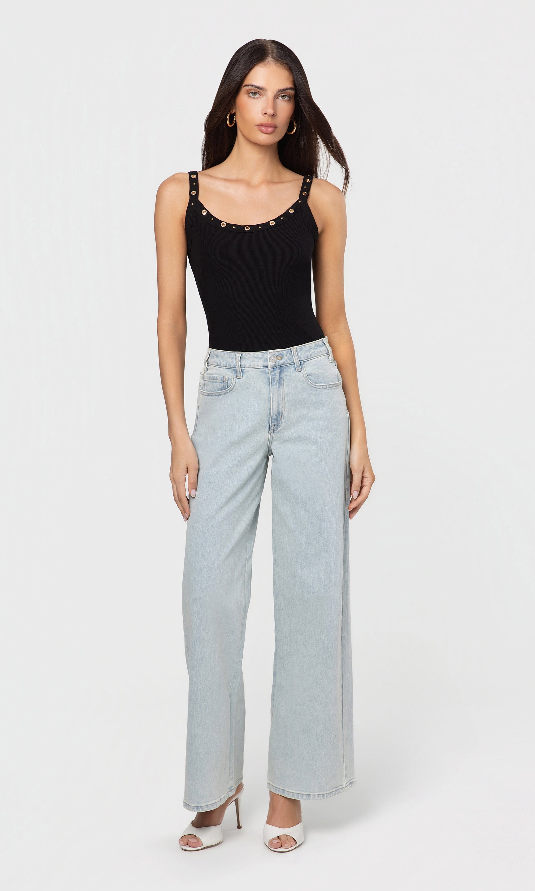 Woman wearing a black studded top and light blue jeans on a white background