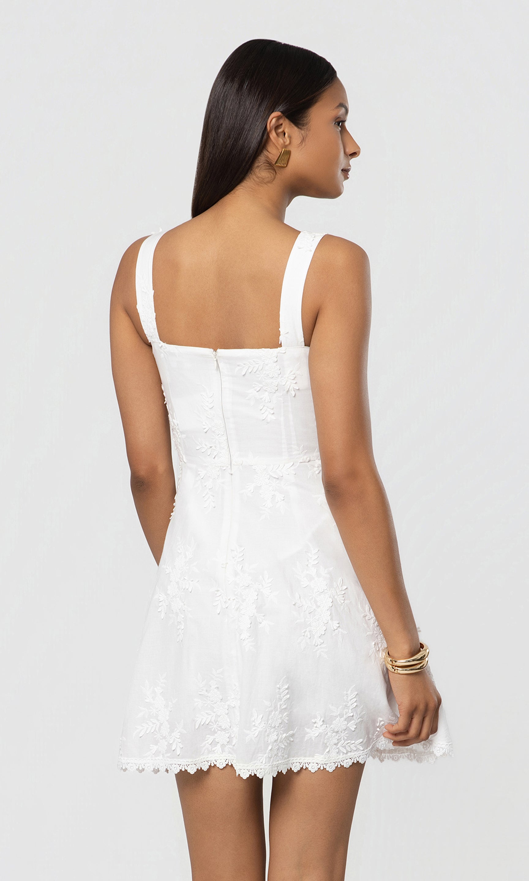 Back view of woman wearing a white lace dress on a plain background