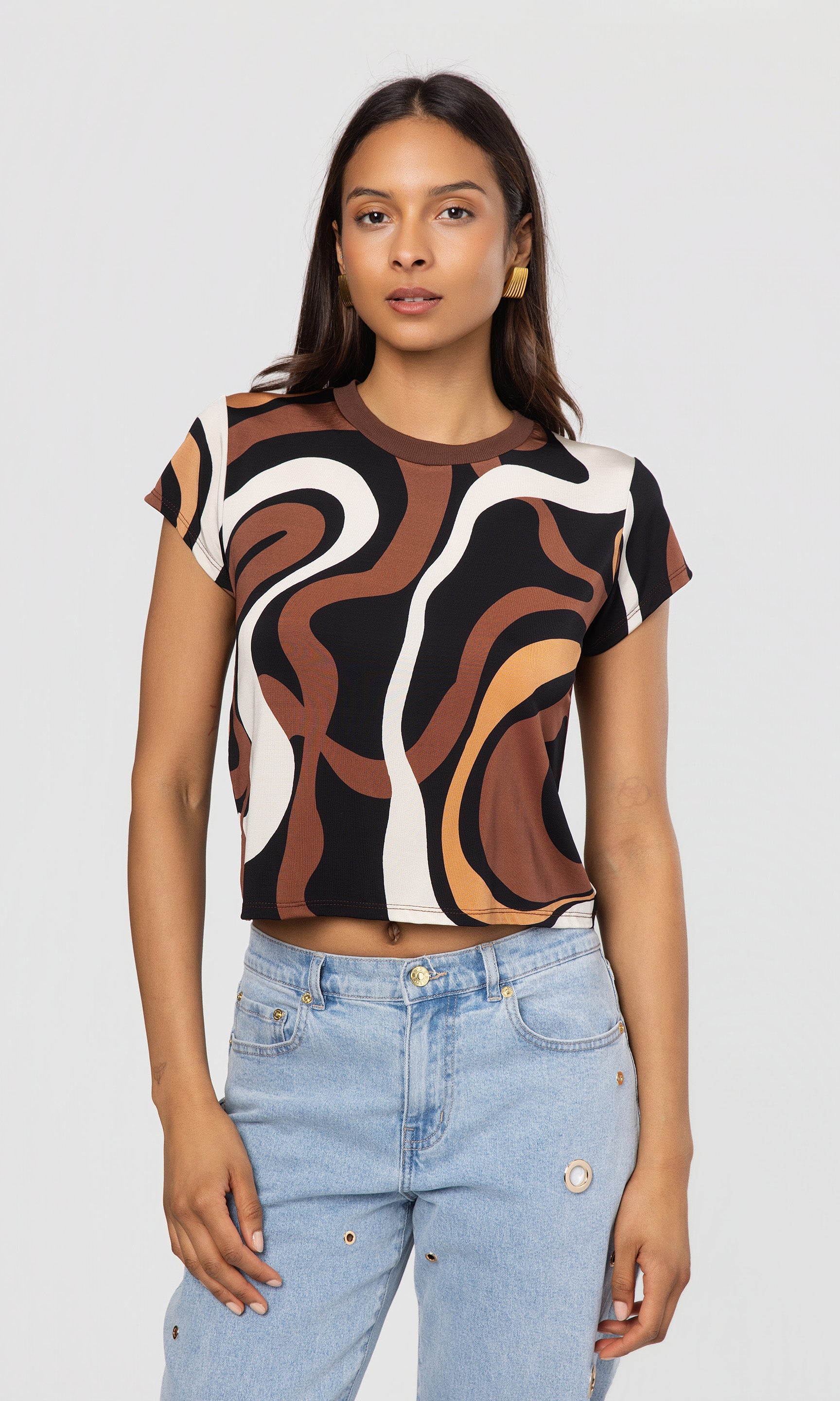 Woman wearing a patterned crop top and jeans on a plain background