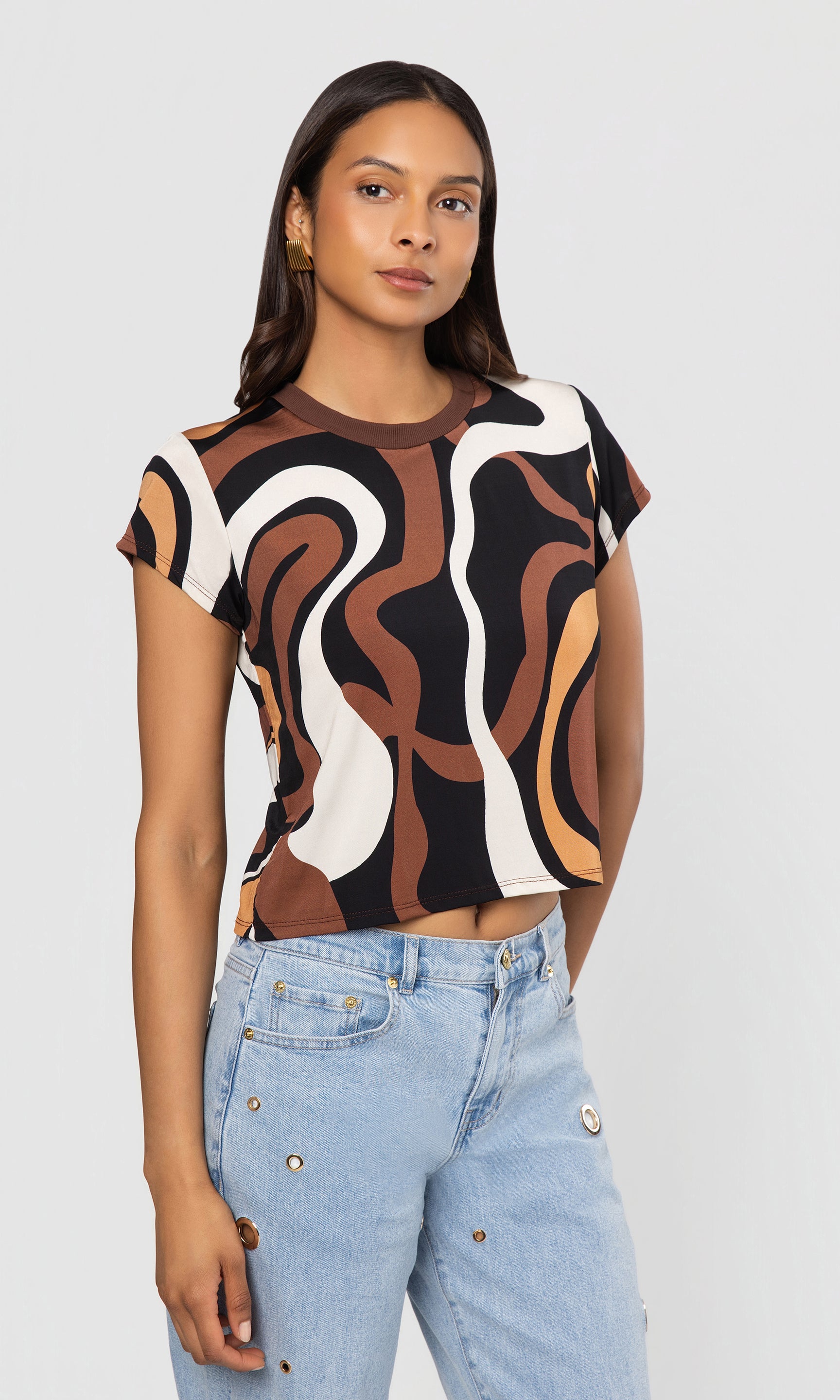 Side view of woman wearing a patterned top and light blue jeans on a plain background