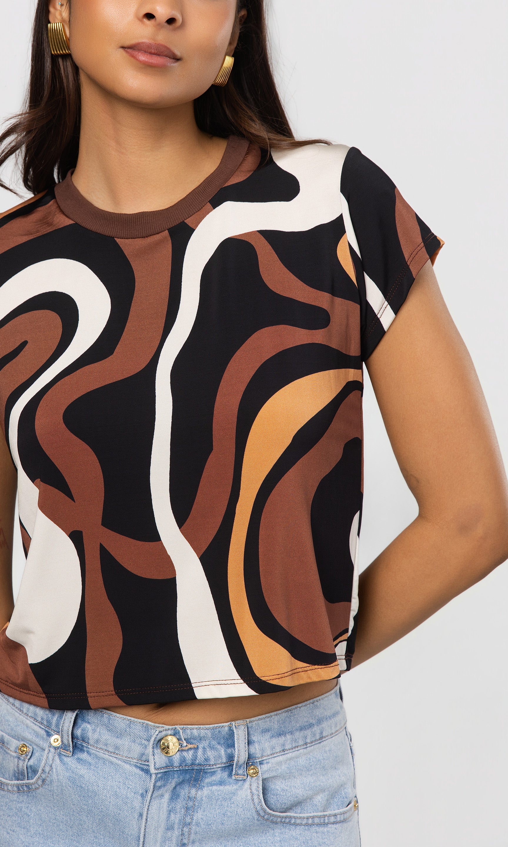 Close-up of woman wearing a brown patterned top with abstract design on a plain background