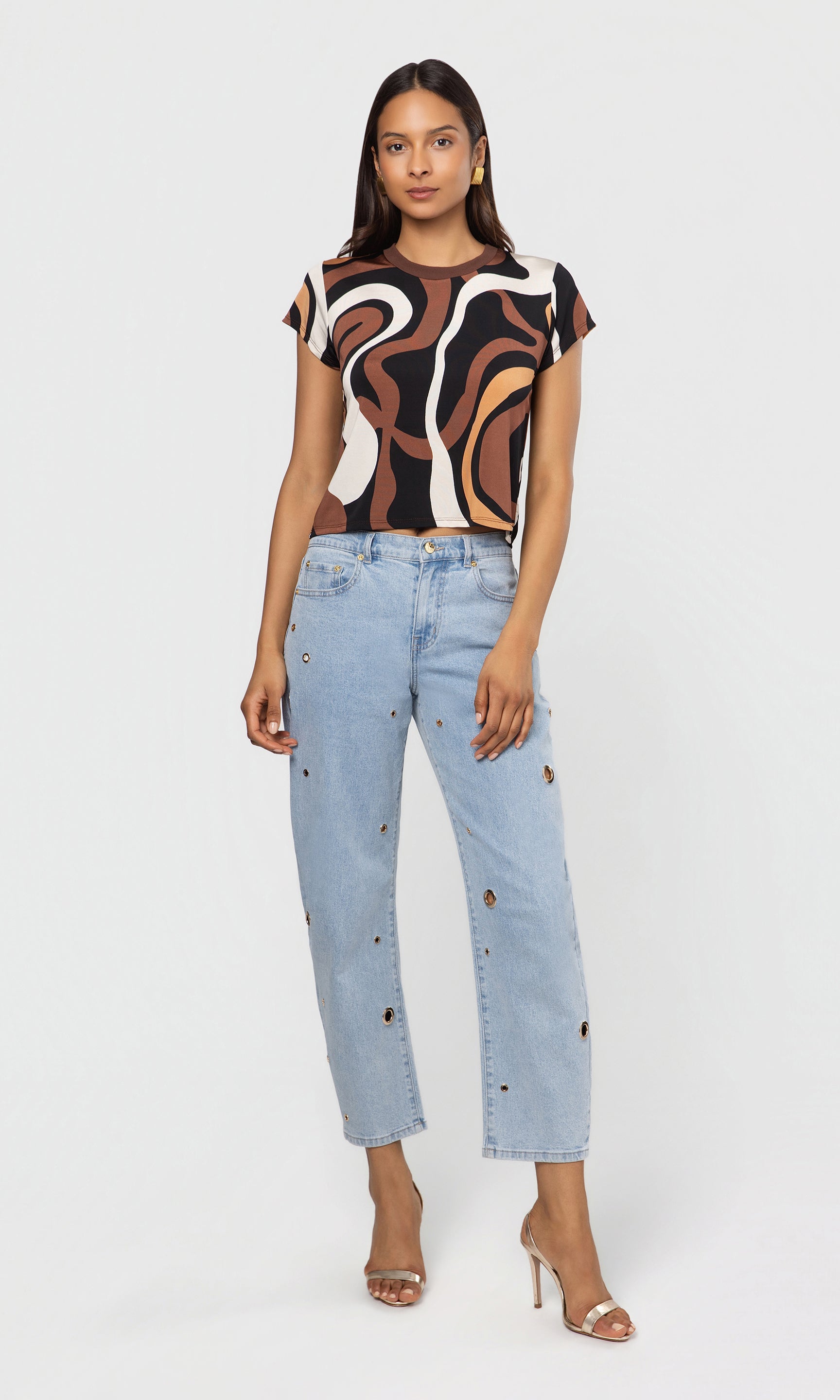 Woman wearing a patterned top and light blue jeans on a white background