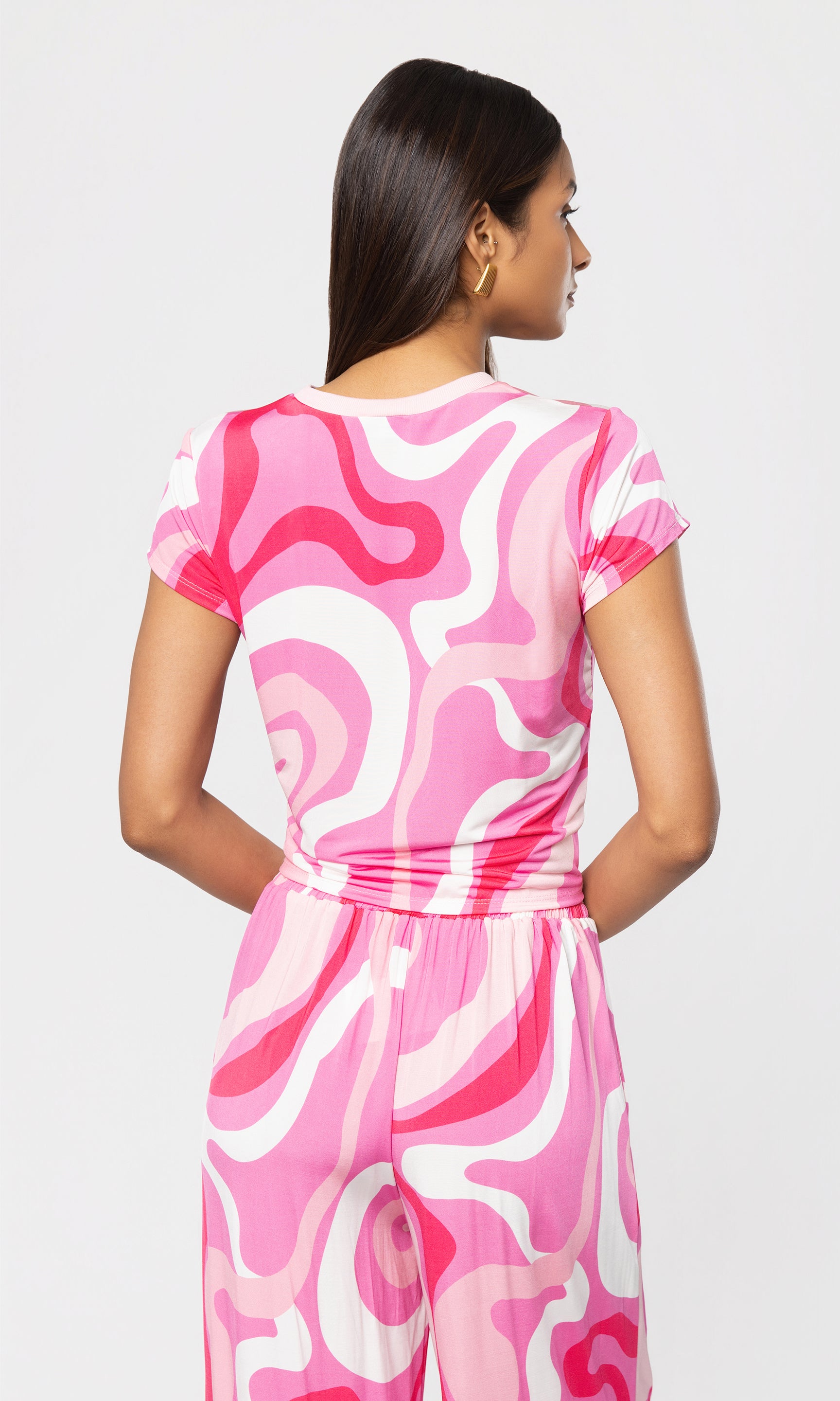 Back view of woman wearing a pink and white patterned top and matching pant on a plain background